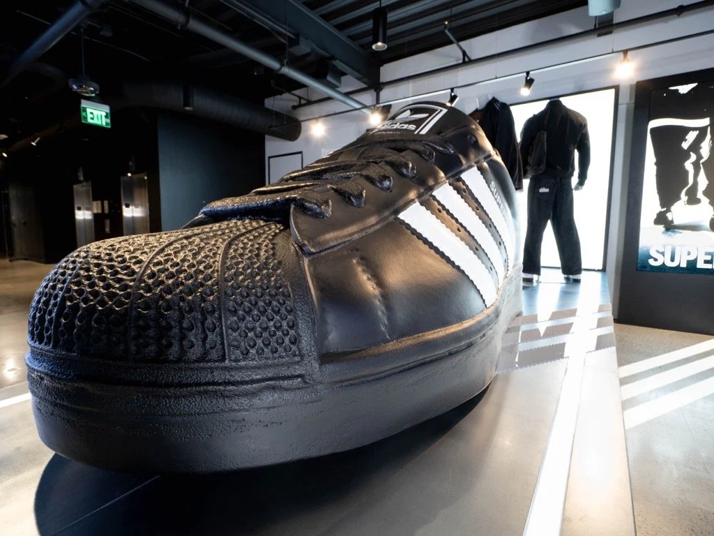 Large black sneaker with white stripes on display inside a store or museum.