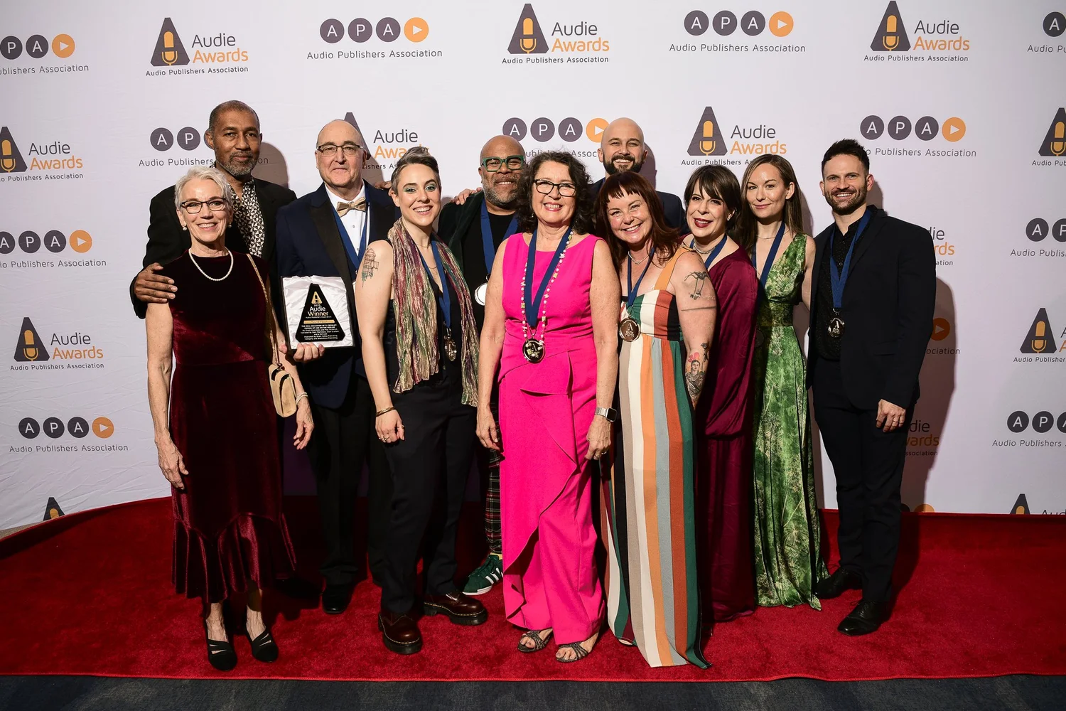 Cast and crew of The Real Education of TJ Crowley holding the Audie Winner plaque in front of an Audio Publishers Association backdrop at the 2025 Audie Awards