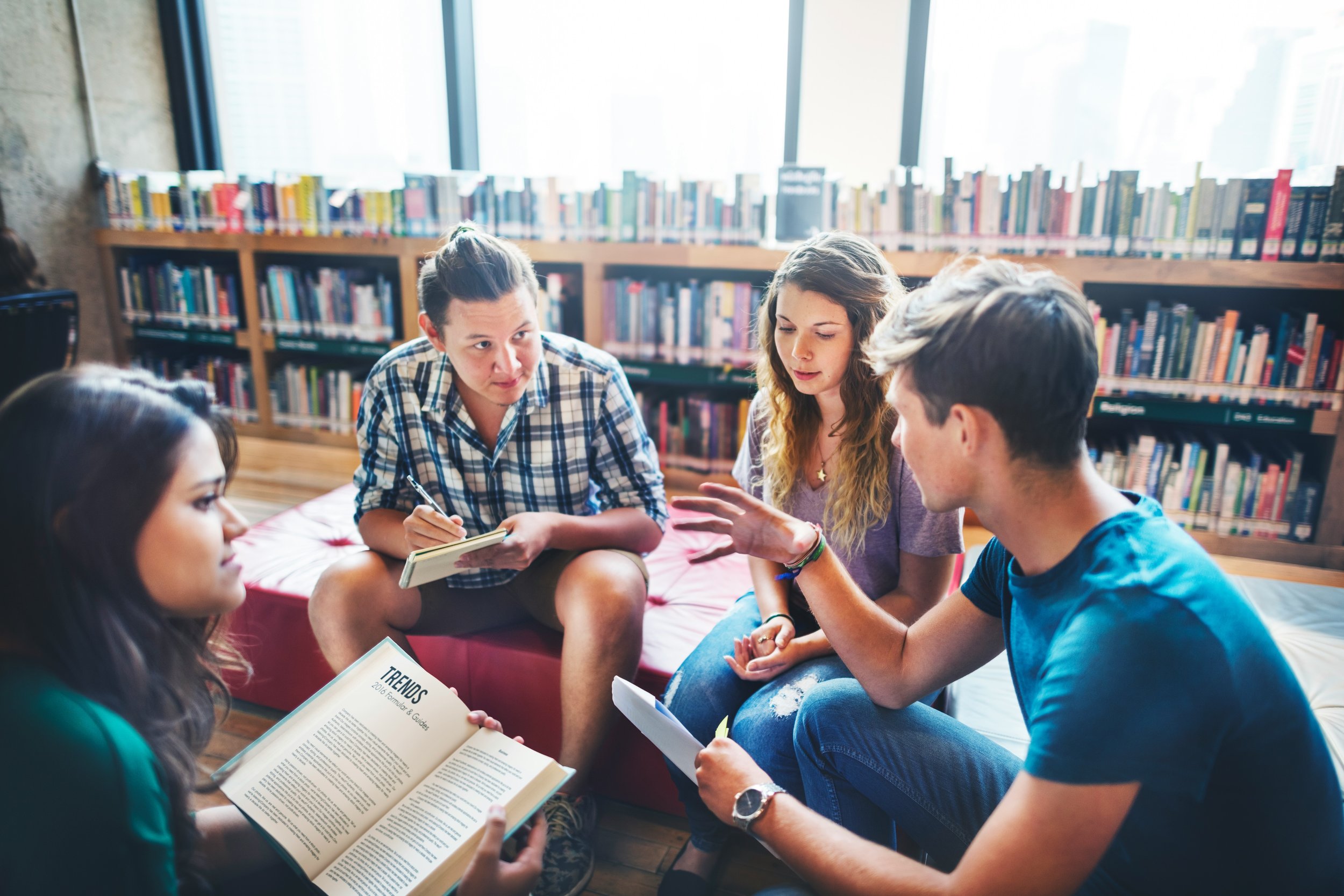 Four college students are in the school library having talking in a small circle.