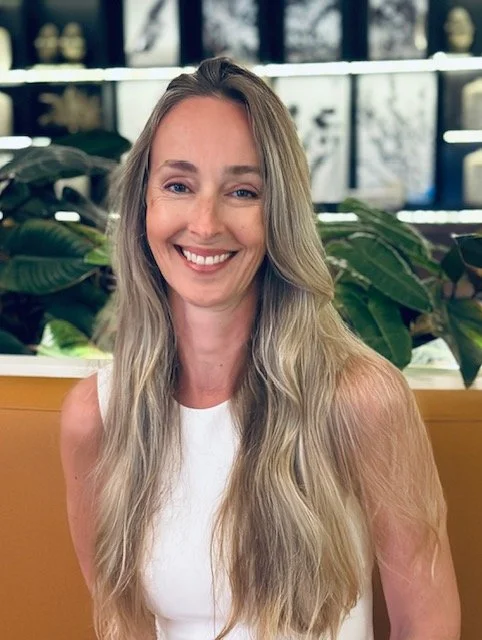 Psychotherapist woman smiling for her head shot in front of green leafy plants.