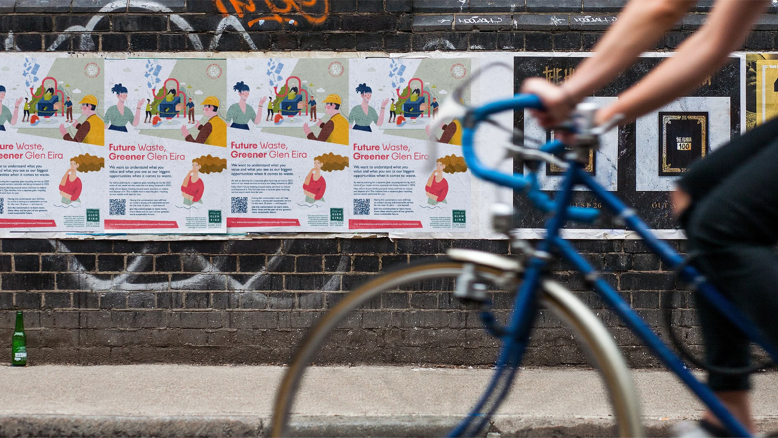 A person riding a blue bicycle past posters on a brick wall, with the posters promoting a waste management campaign in Glen Eira, Australia.