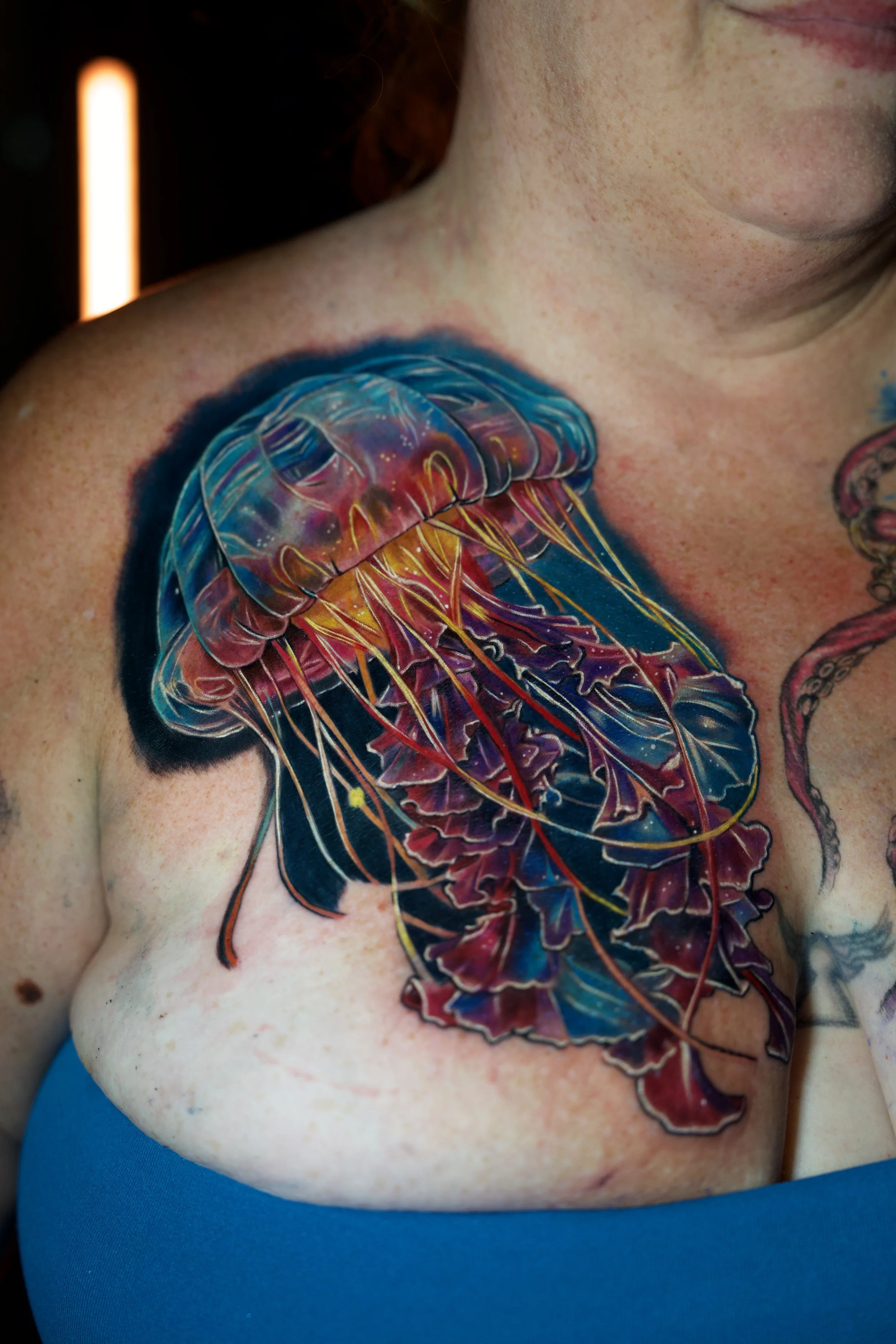 Colorful jellyfish tattoo on person's shoulder and chest with vibrant blues, reds, and yellows.