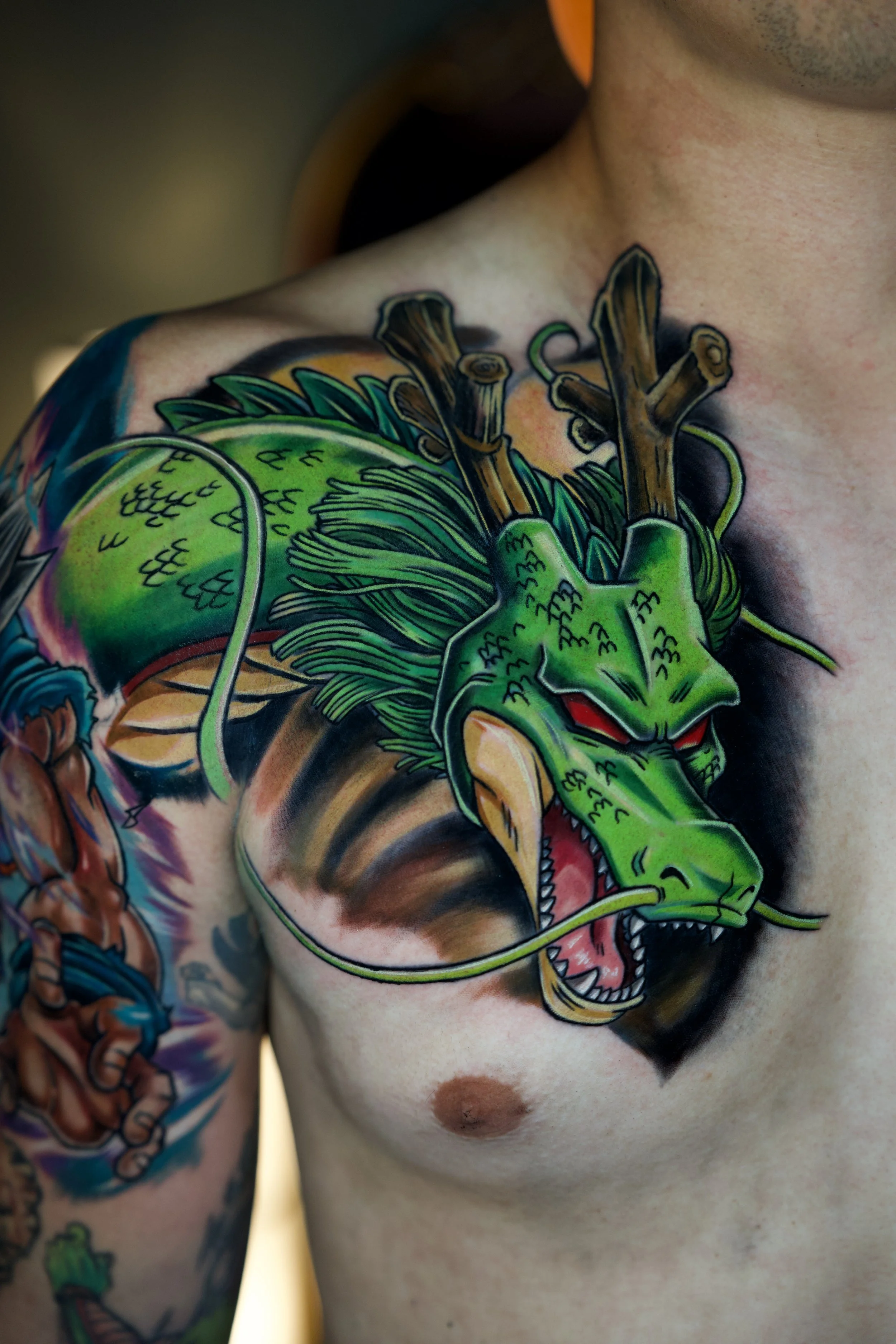Colorful tattoo of Shenron, the green dragon from Dragon Ball Z, on man's chest with a background of other tattoos.