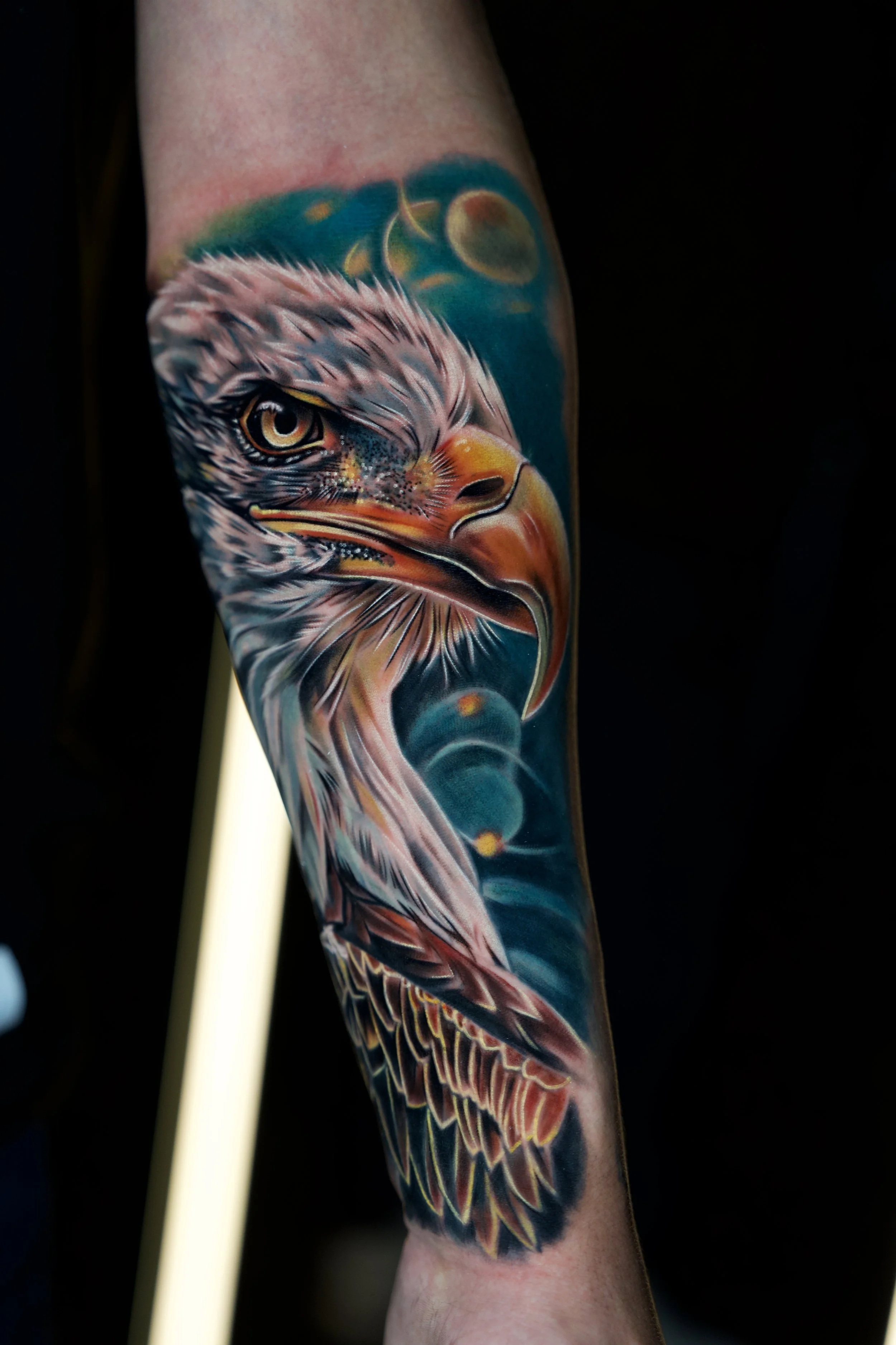 Colorful tattoo of an eagle's head on a person's arm with a dark background and a bokeh background.