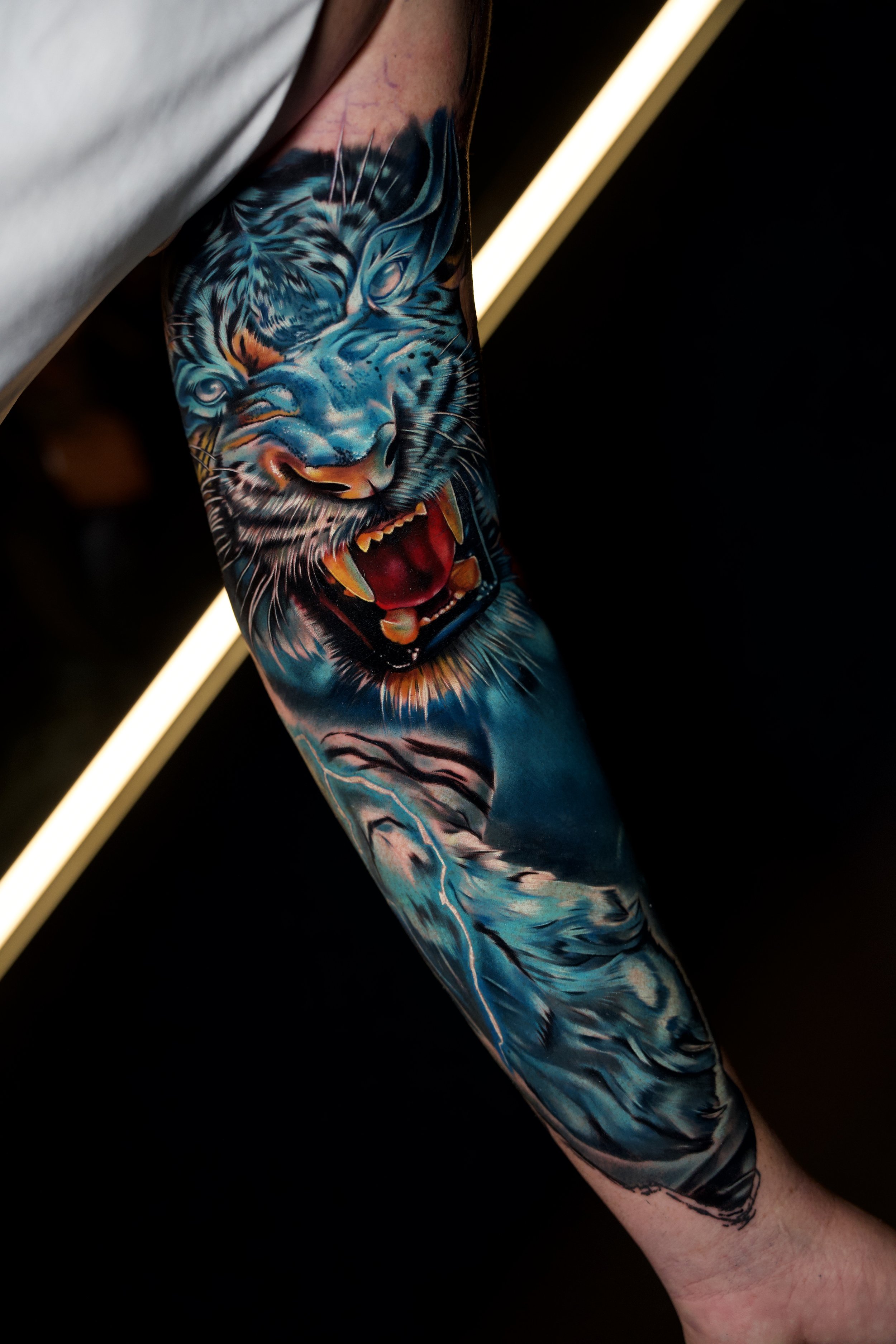 Close-up of a colorful tattoo of a roaring tiger on a person's arm, featuring vibrant blues, oranges, and reds.