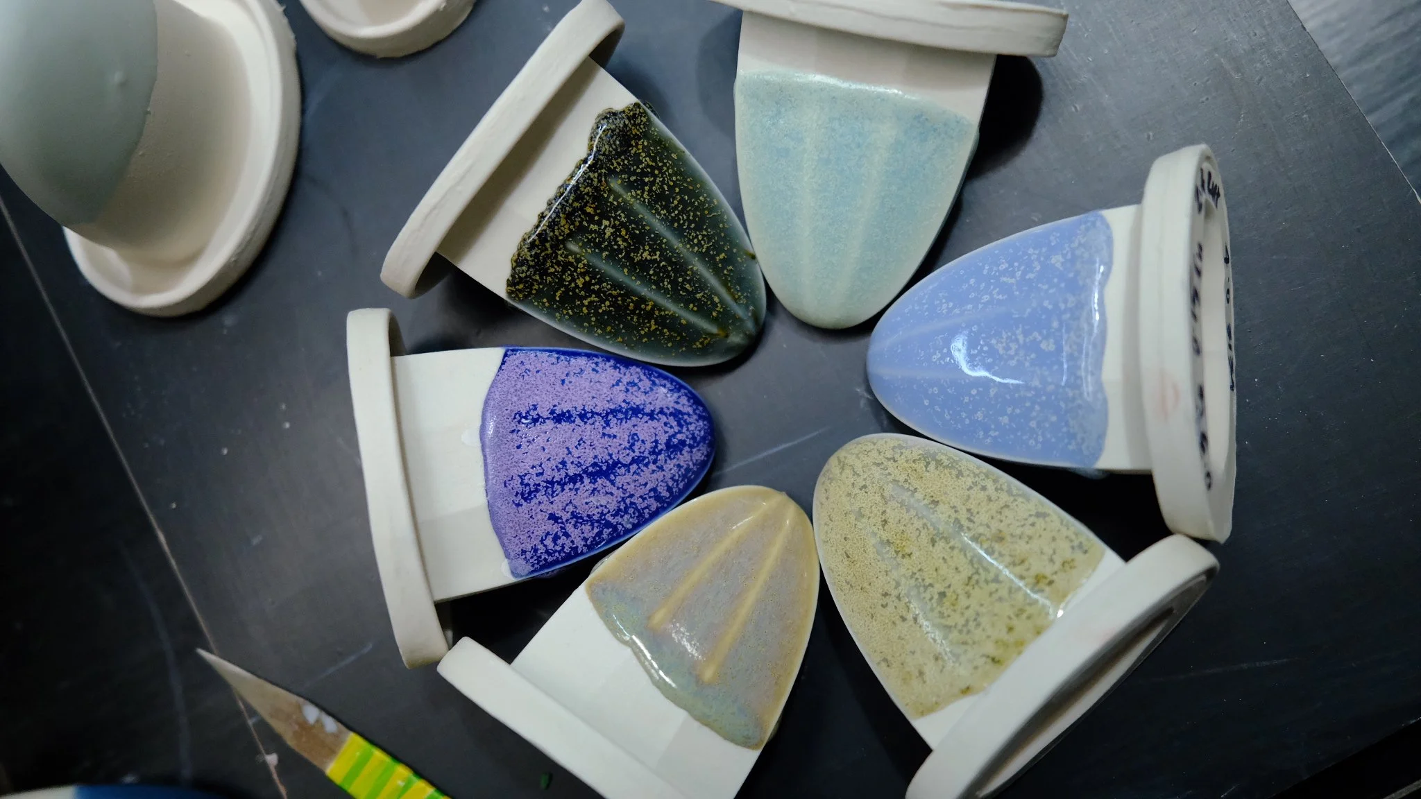 Several ceramic planters with colorful glazes, arranged on a dark surface. The planters are small, conical, and have a decorative design with various pastel and darker hues.