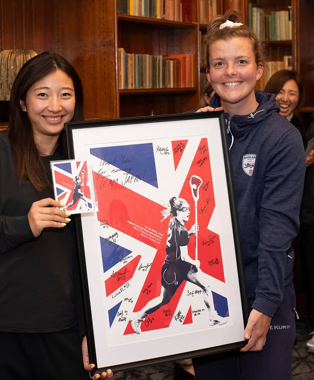 A member of the Japan lacrosse squad and an England player holding the signed and framed England Lacrosse poster together.