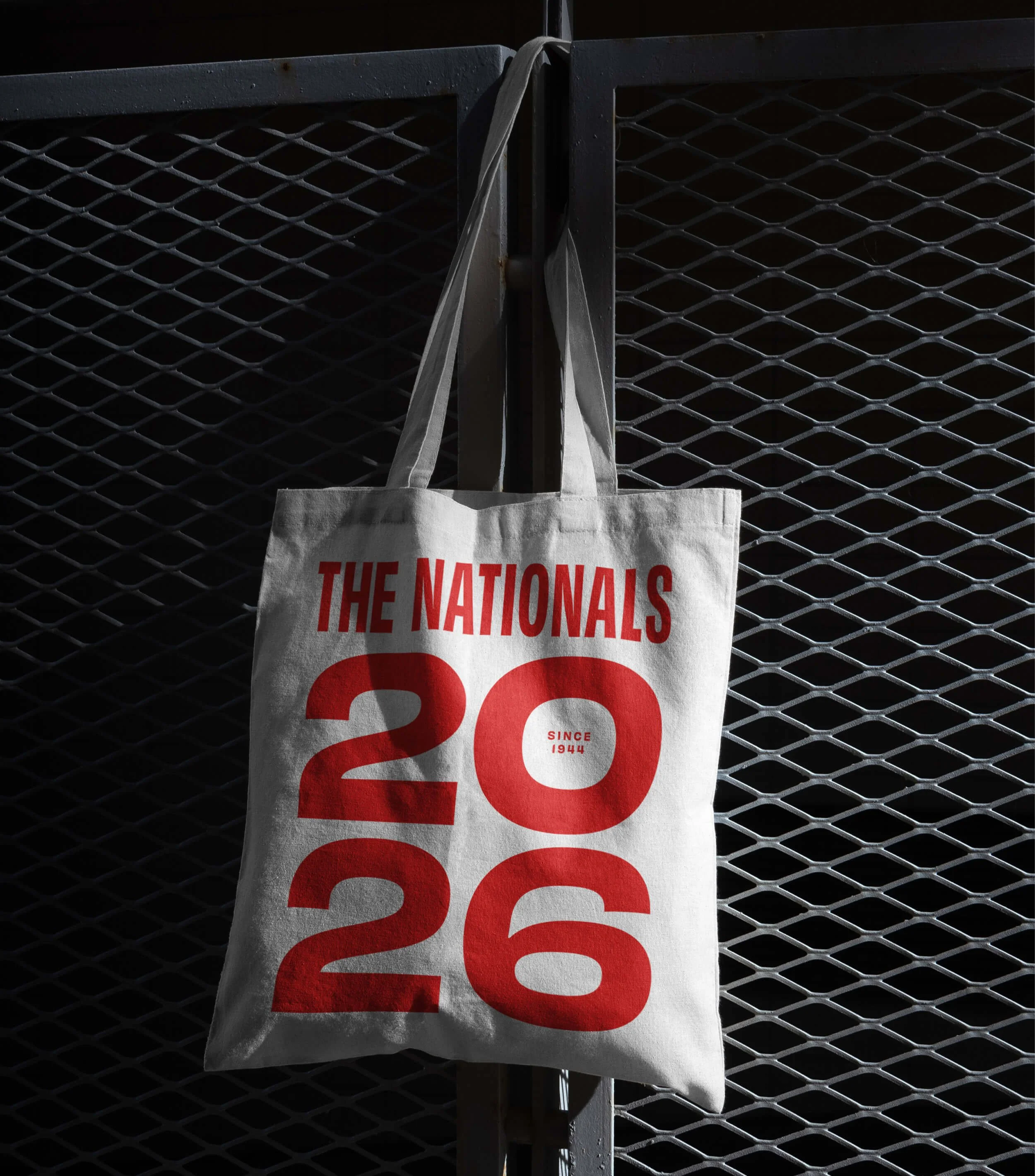 A tote bag hanging on a metal fence displaying the Nationals 2026 logo.