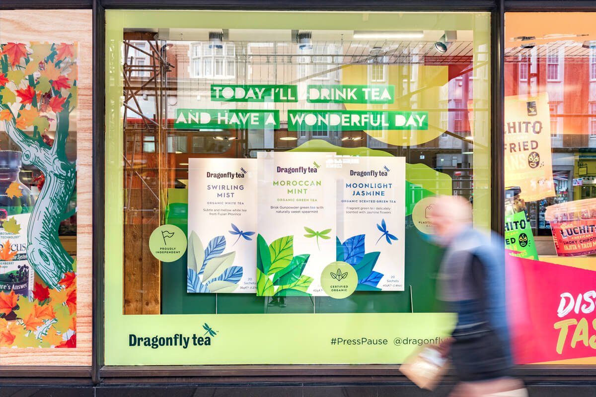 A man walking past a window with advertising for Dragonfly Tea.