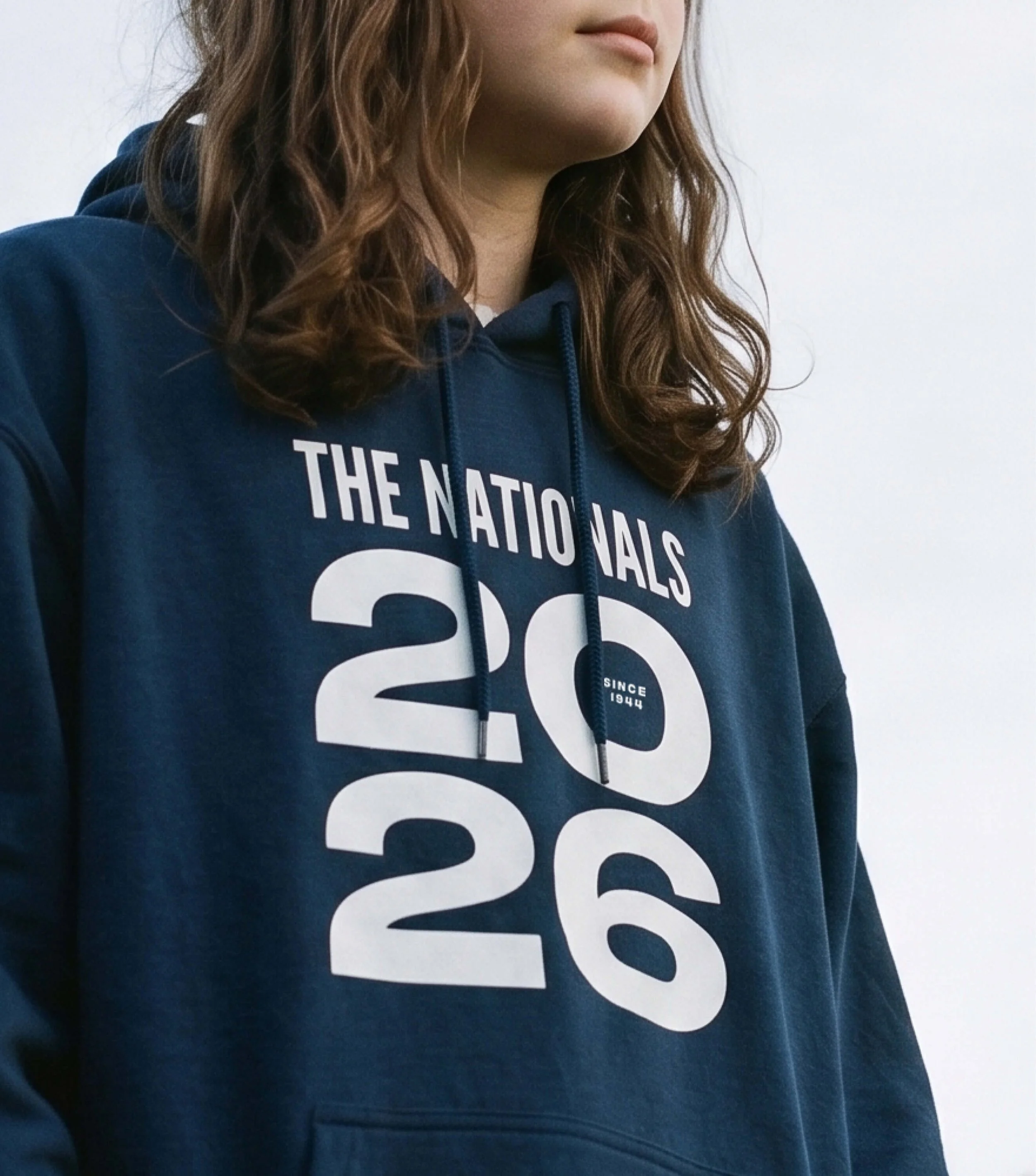 A girl wearing a dark blue hoodie showing the design for the Nationals 2026.