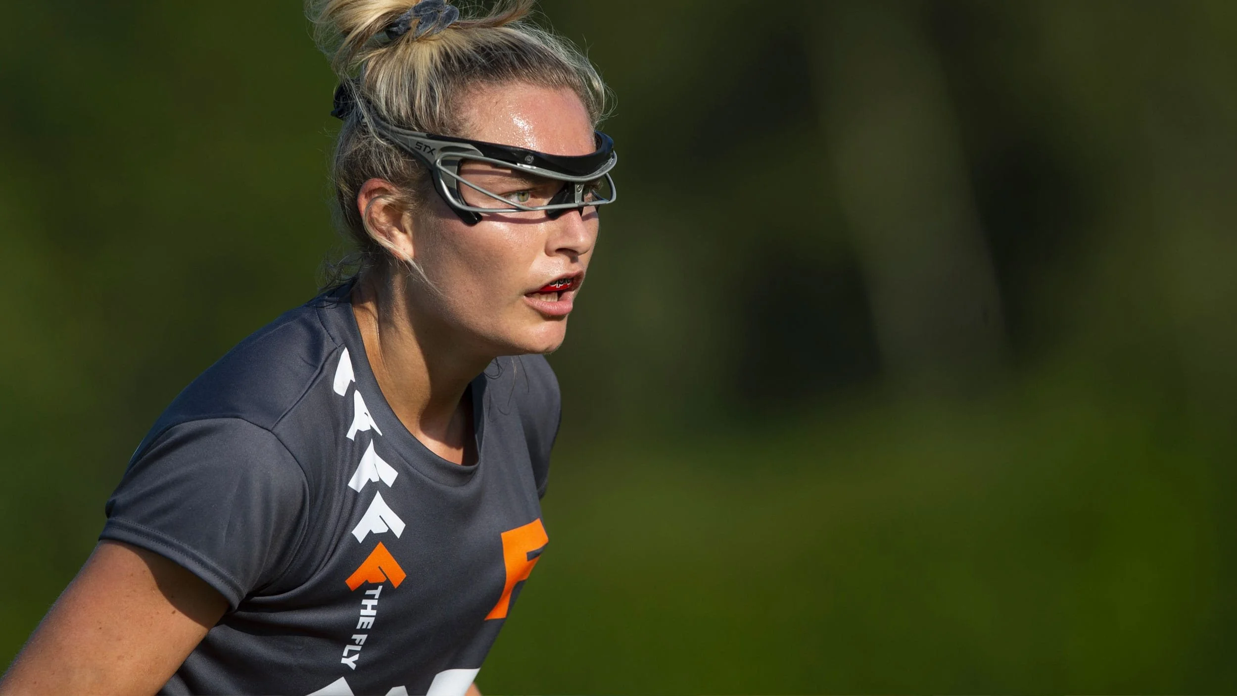Close up of a lacrosse player with The Fly logo on her black jersey.