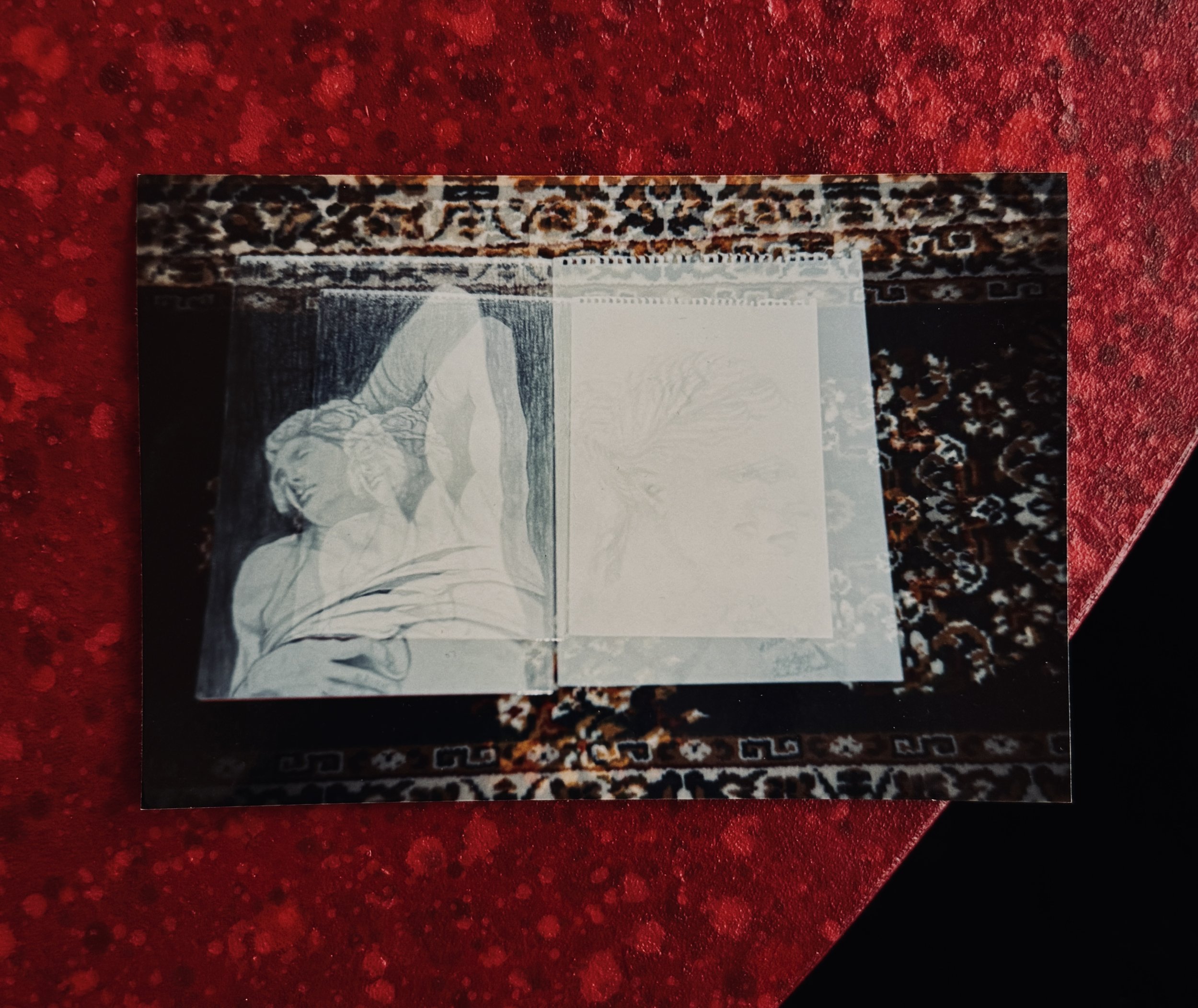 Analogue photograph of an open sketchbook placed on a patterned carpet, showing a pencil study after Michelangelo’s Dying Slave. The image appears softly blurred and partially overexposed, with the drawing on the right barely visible.