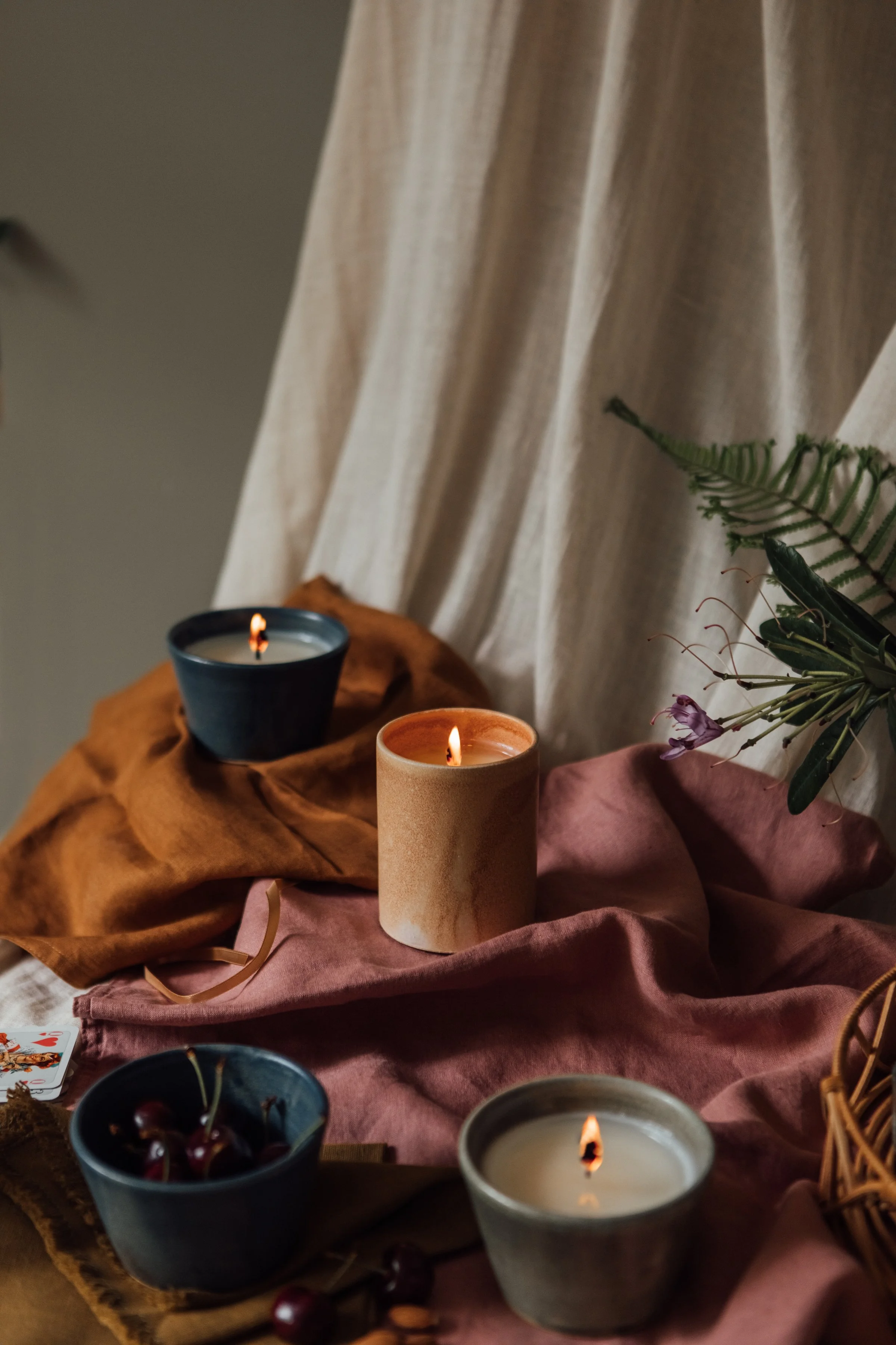 Lit candles with cherries and greenery on draped fabrics