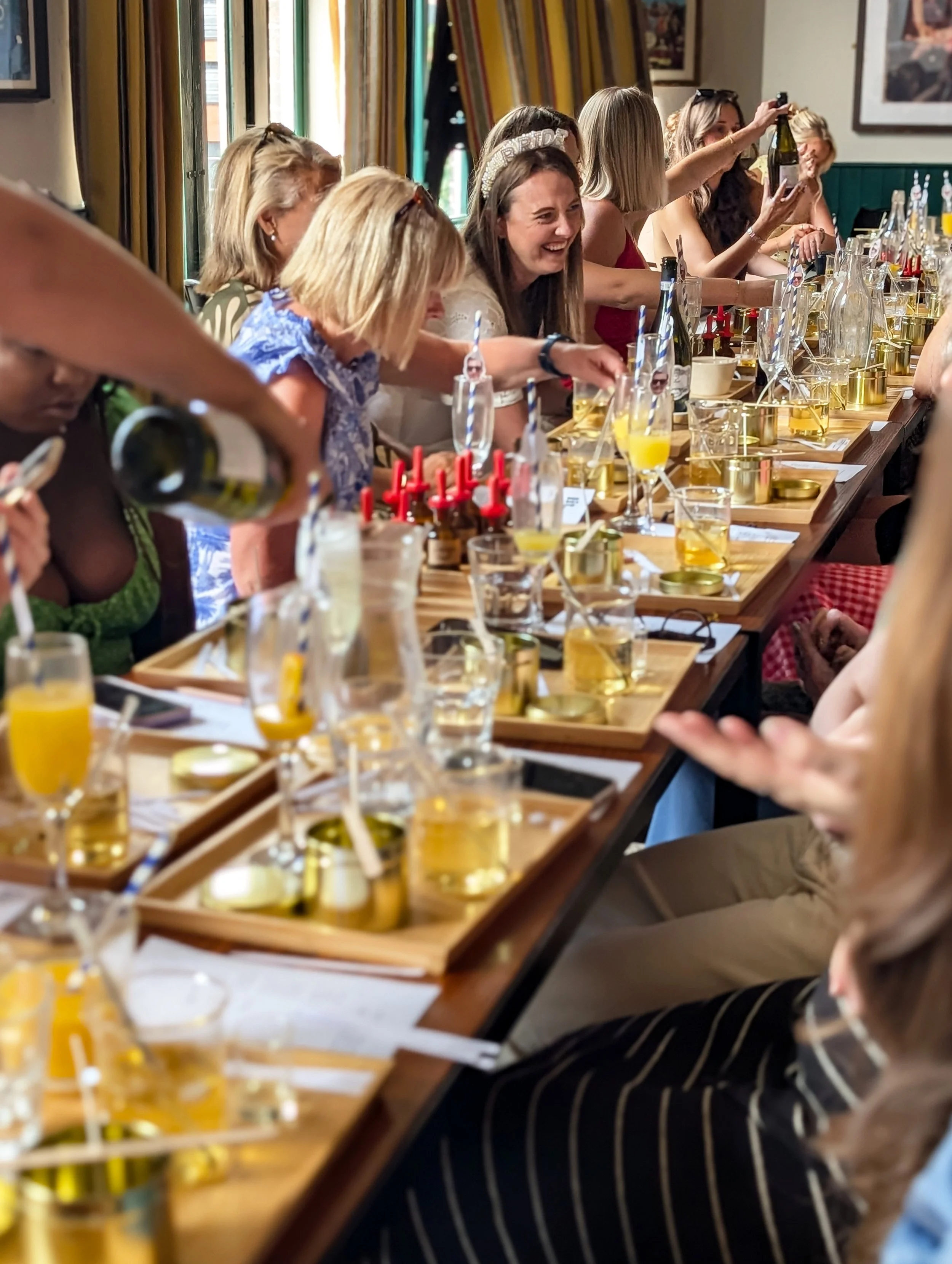 Hen Party enjoying a candle making workshop, champagne being poured in the foreground, bride to be laughing in the background.