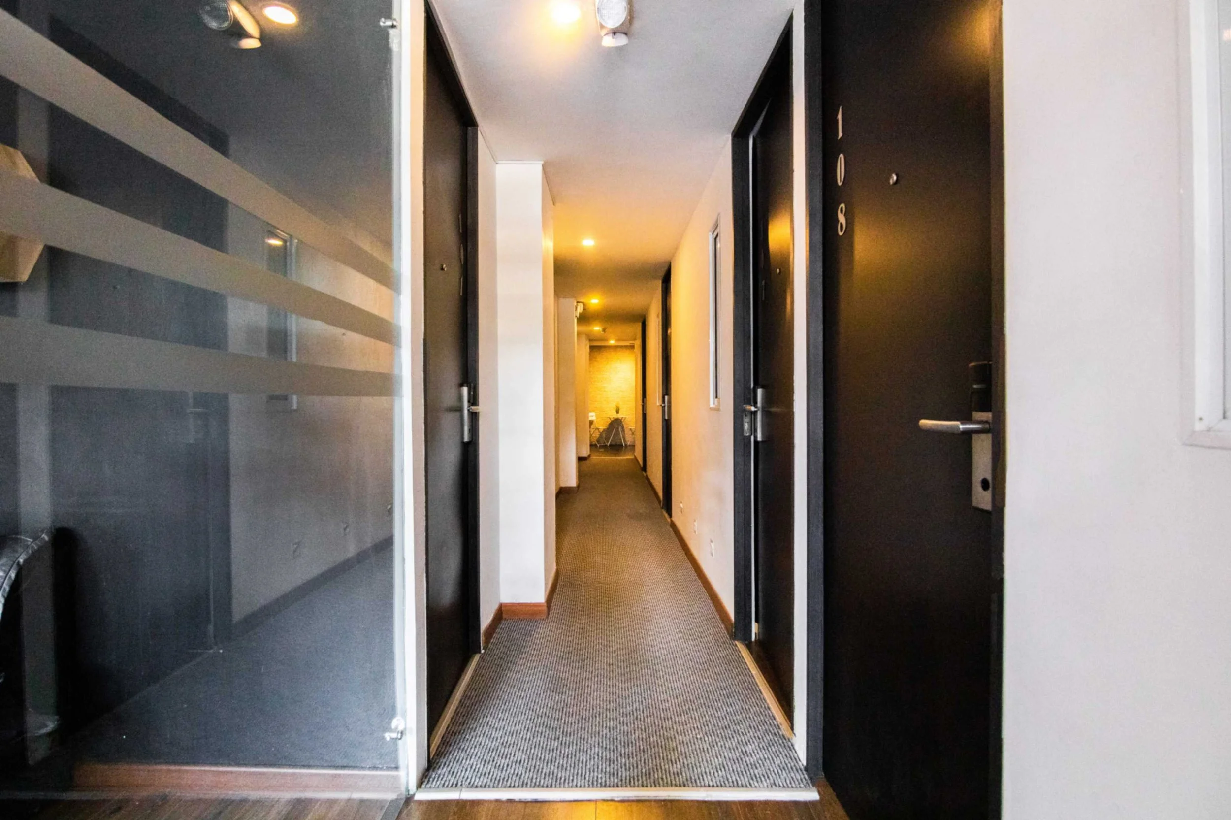Pasillo de hotel con puertas negras numeradas y alfombra gris.