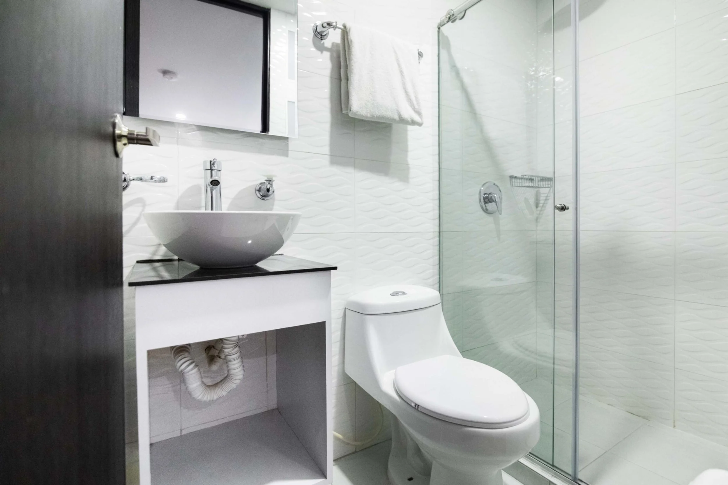 Baño con ducha de vidrio, inodoro, lavabo sobre mueble y espejo.