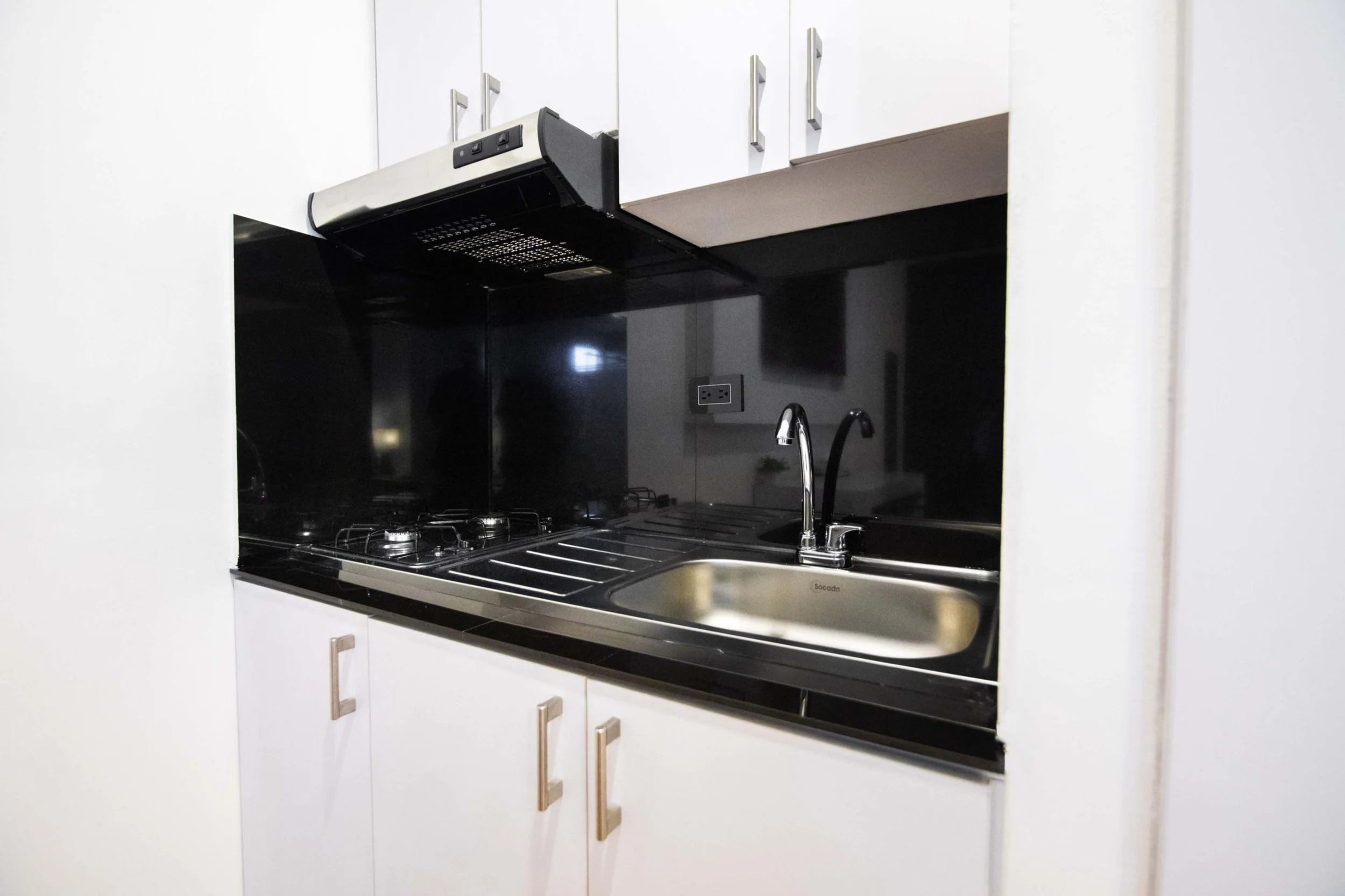 Cocina moderna con estufa de gas, fregadero y armarios blancos.