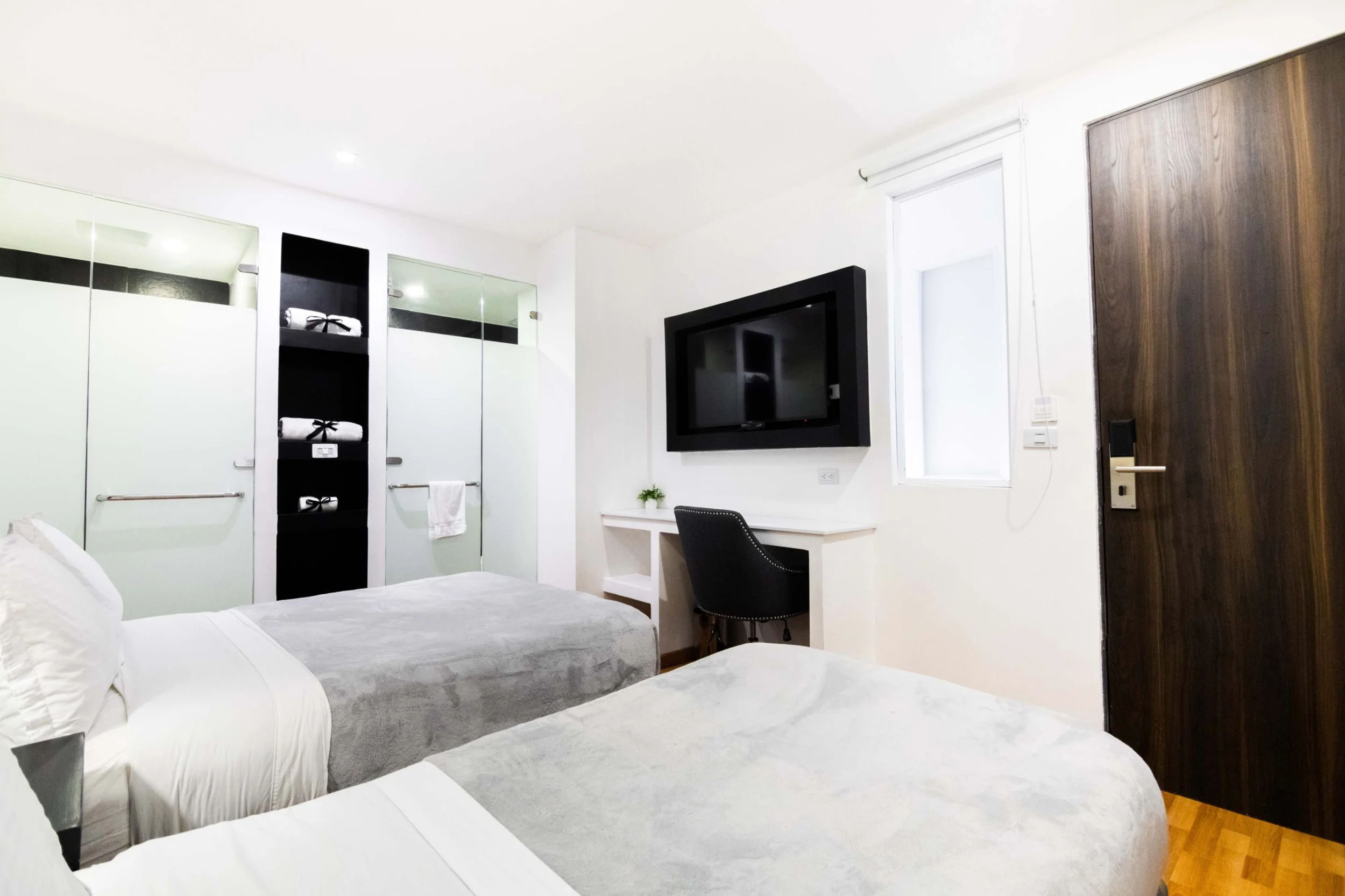 Habitación con dos camas, armarios con puertas de cristal, televisión en la pared, escritorio con silla y ventana con cortina.