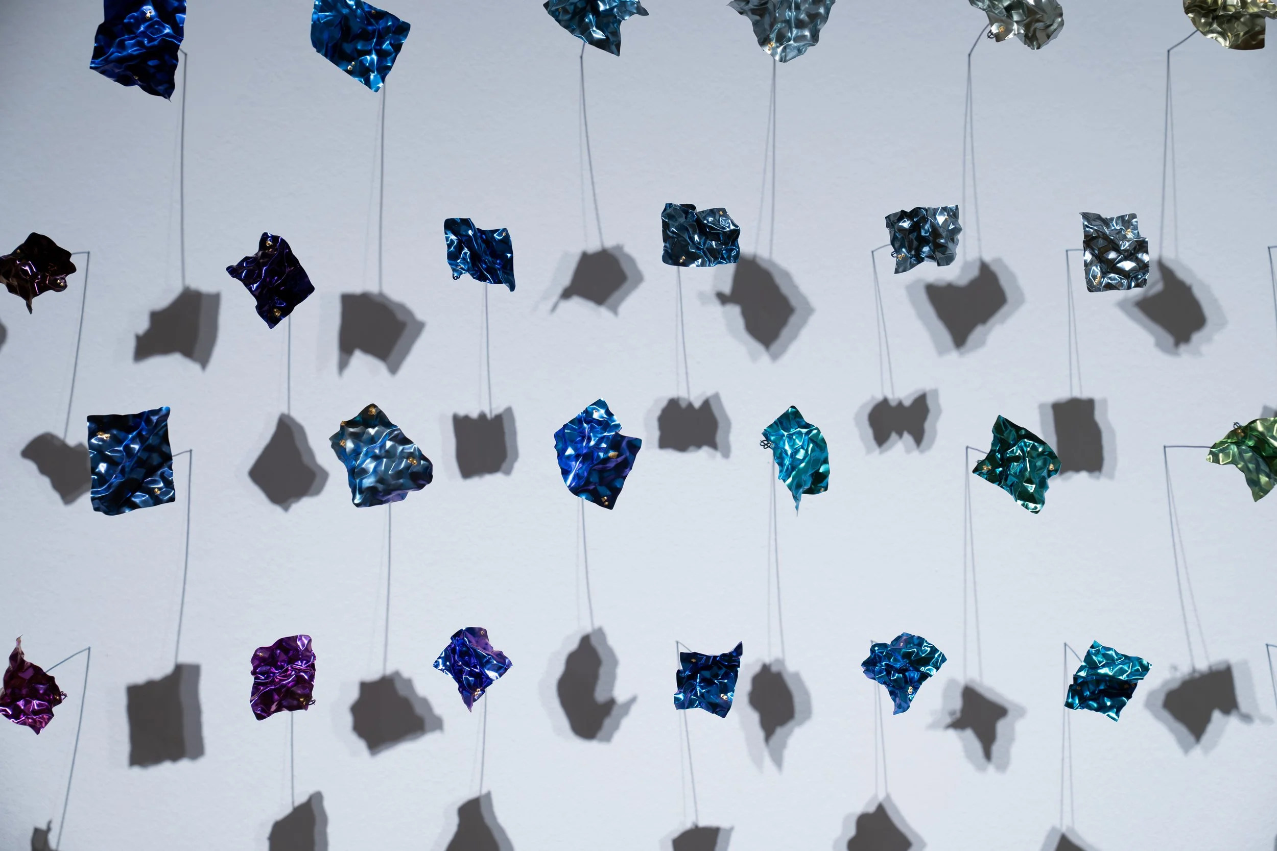 Weiwei Li, 
Quiet Fragments, 
2026, 
Titanium, niobium, gold foil. 
38 individual pieces. 
 55" x 17" x 6"