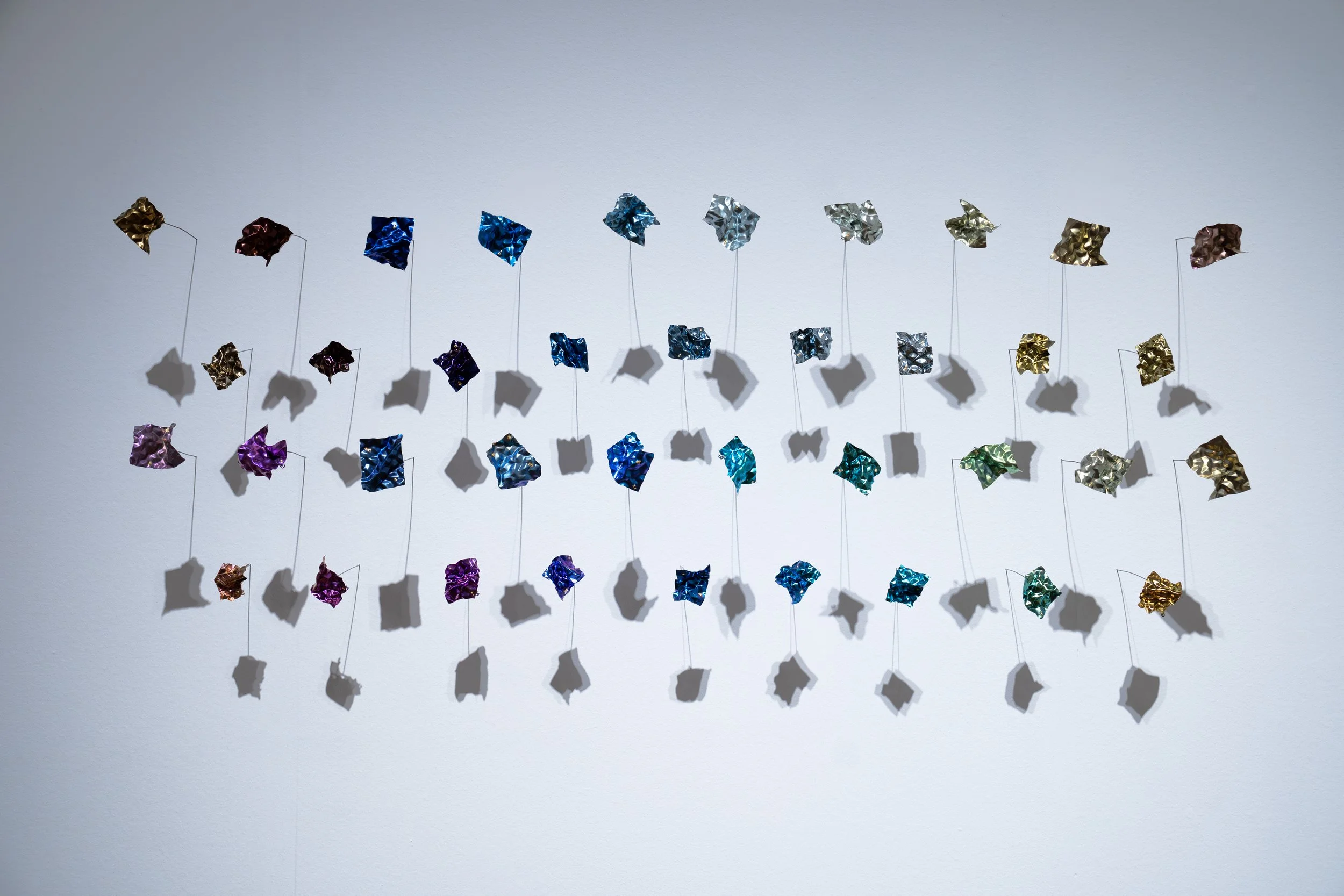 Weiwei Li, 
Quiet Fragments, 
2026, 
Titanium, niobium, gold foil. 
38 individual pieces. 
 55" x 17" x 6" 