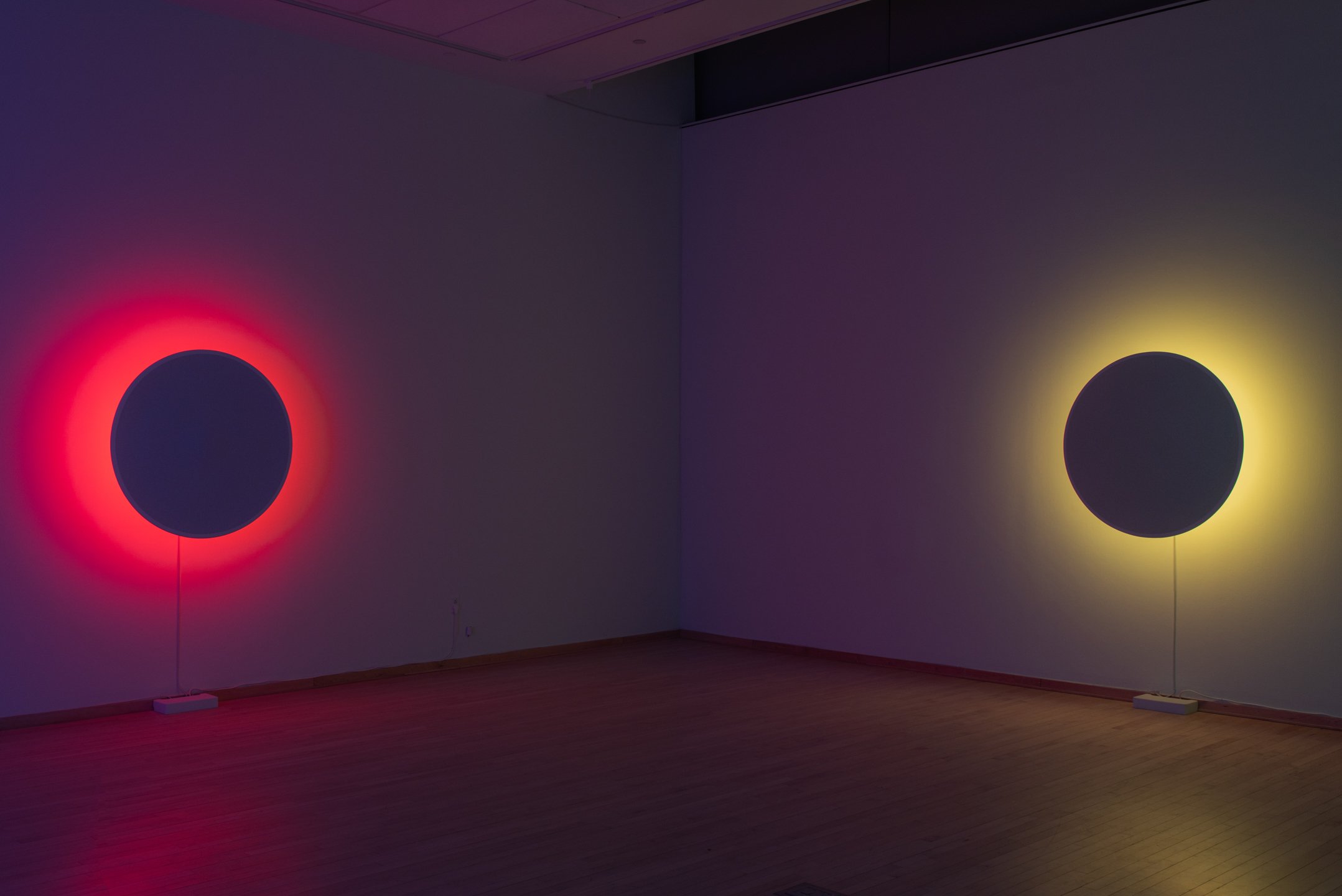 "In Totality" (still), 2025, Time-based installation view showing “Optic Disc (Red)” and “Optic Disc (Yellow),” Retroreflective glass microspheres, acrylic paint, foam, steel, LED light, computer controller. 46” by 46” by 14” each, Photo credit: Neig
