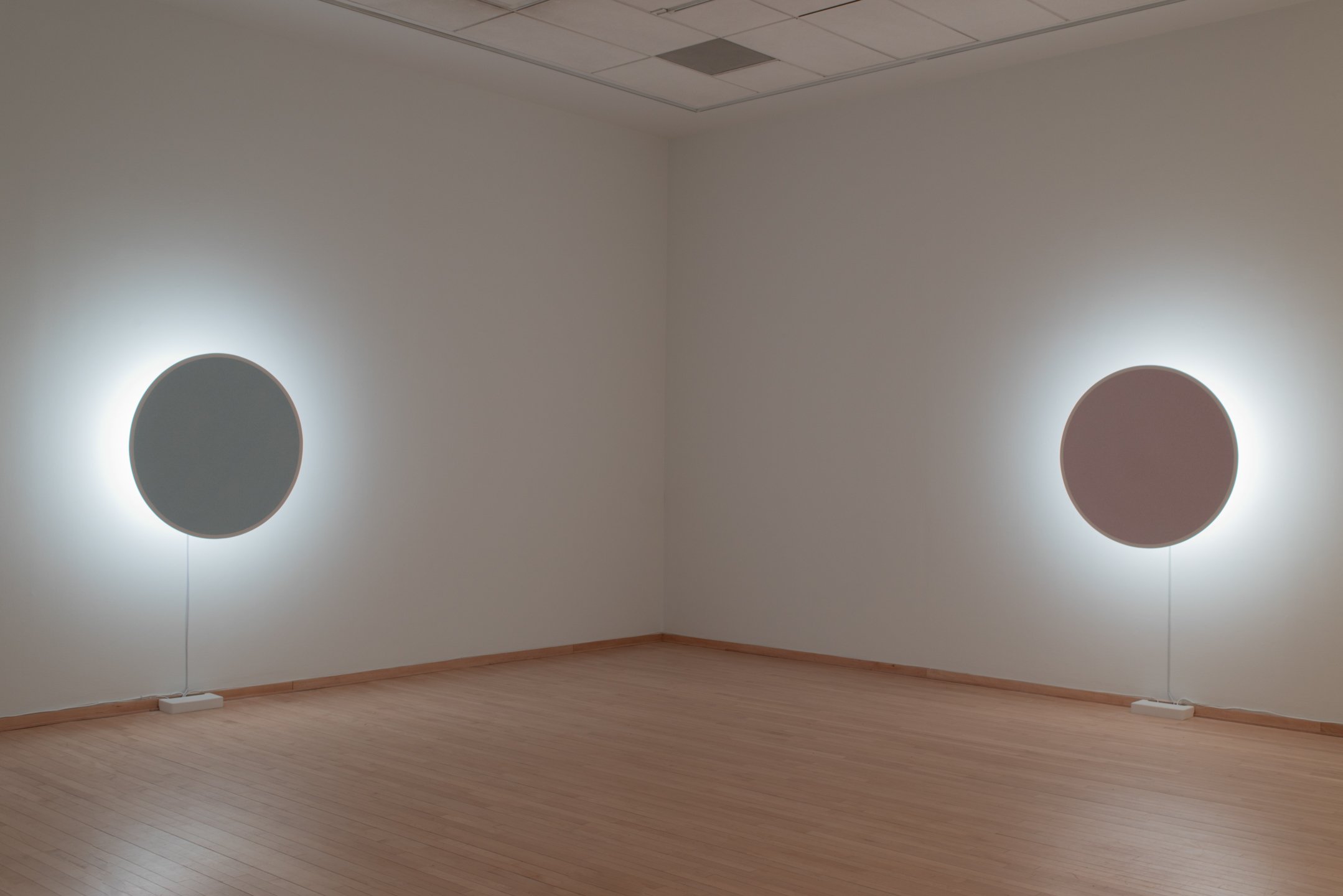 "In Totality" (still), 2025, Time-based installation view showing “Optic Disc (Red)” and “Optic Disc (Yellow),” Retroreflective glass microspheres, acrylic paint, foam, steel, LED light, computer controller. 46” by 46” by 14” each, Photo credit: Neig