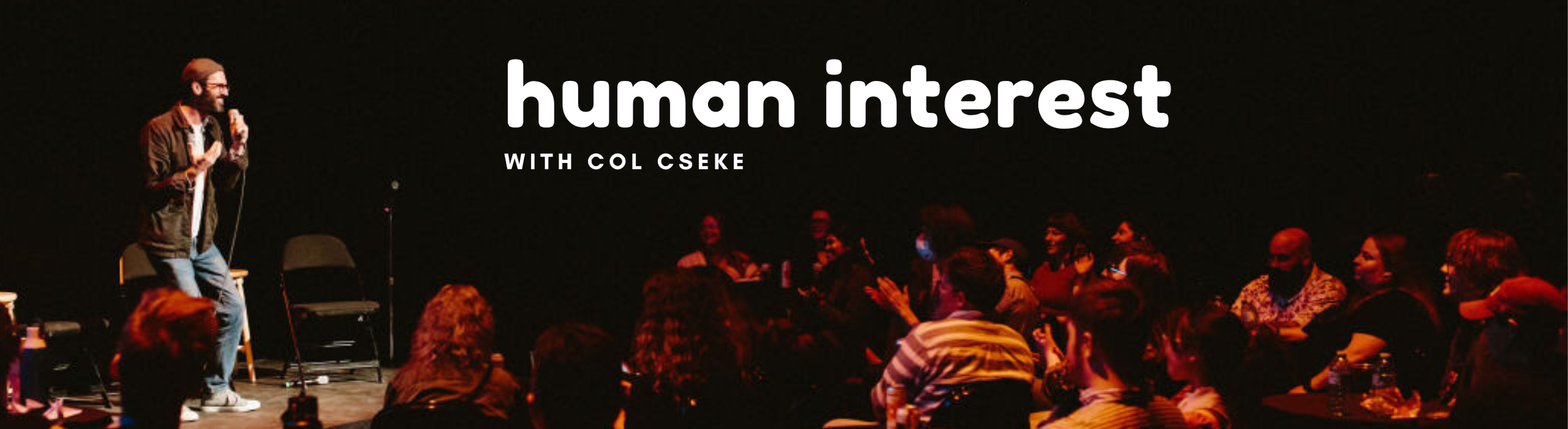 Host Col Cseke stands onstage, microphone in hand, in front of an audience