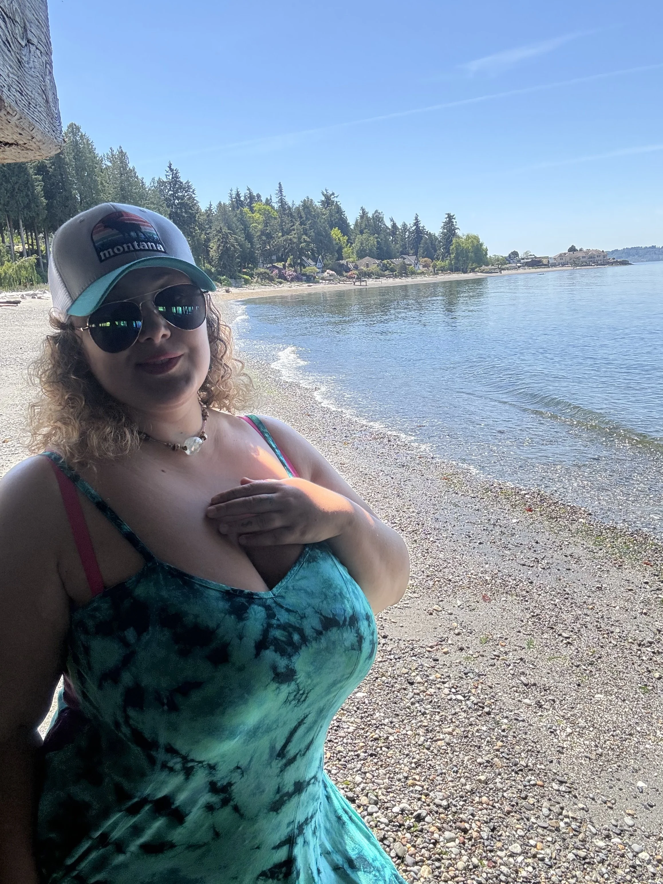 Arianna at the beach, wearing a 'Montana' trucker hat and green tie-dye dress,