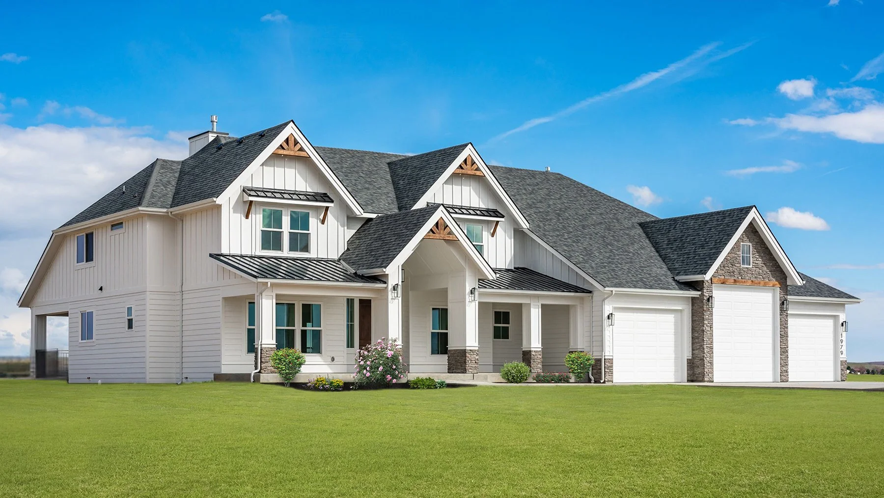 A large modern house with white siding, dark gray roof, and stone accents, surrounded by a green lawn and blue sky.