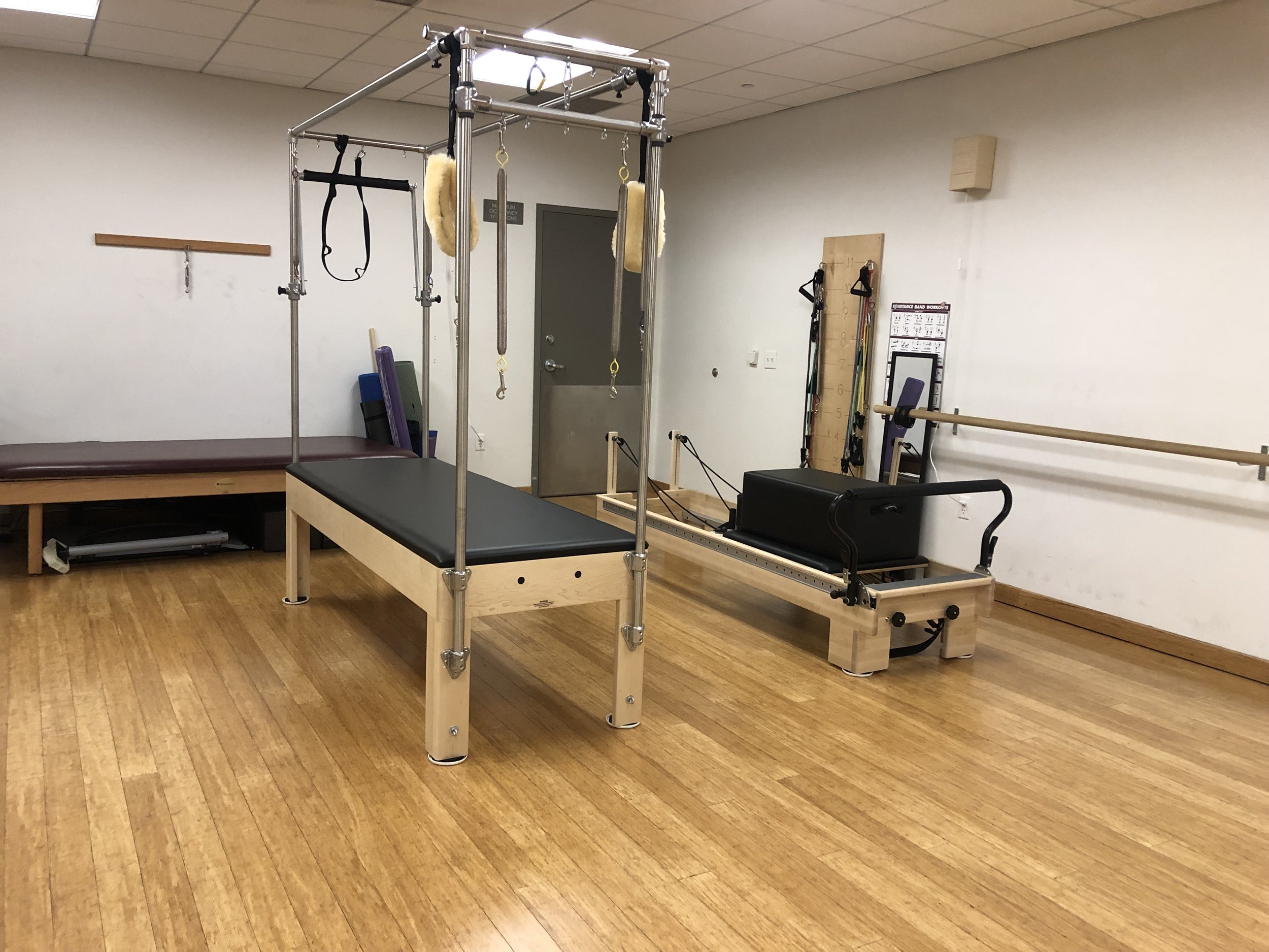 Pilates trapeze table and pilates reformer next to each other in fitness studio with hardwood floors
