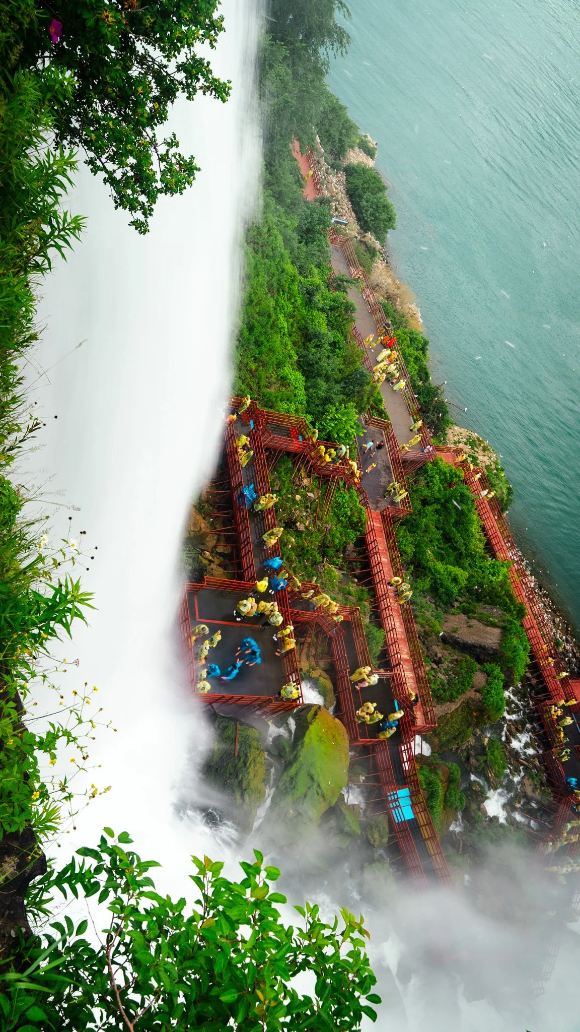 A waterfall with a viewing platform and people wearing raincoats