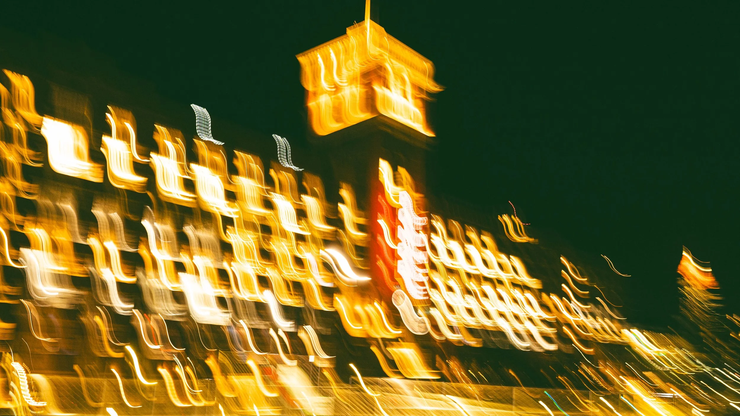 Ponce City Market - Blurred city lights at night creating streaks of yellow, white, and red against a dark sky, with a prominent illuminated building or tower in the center.