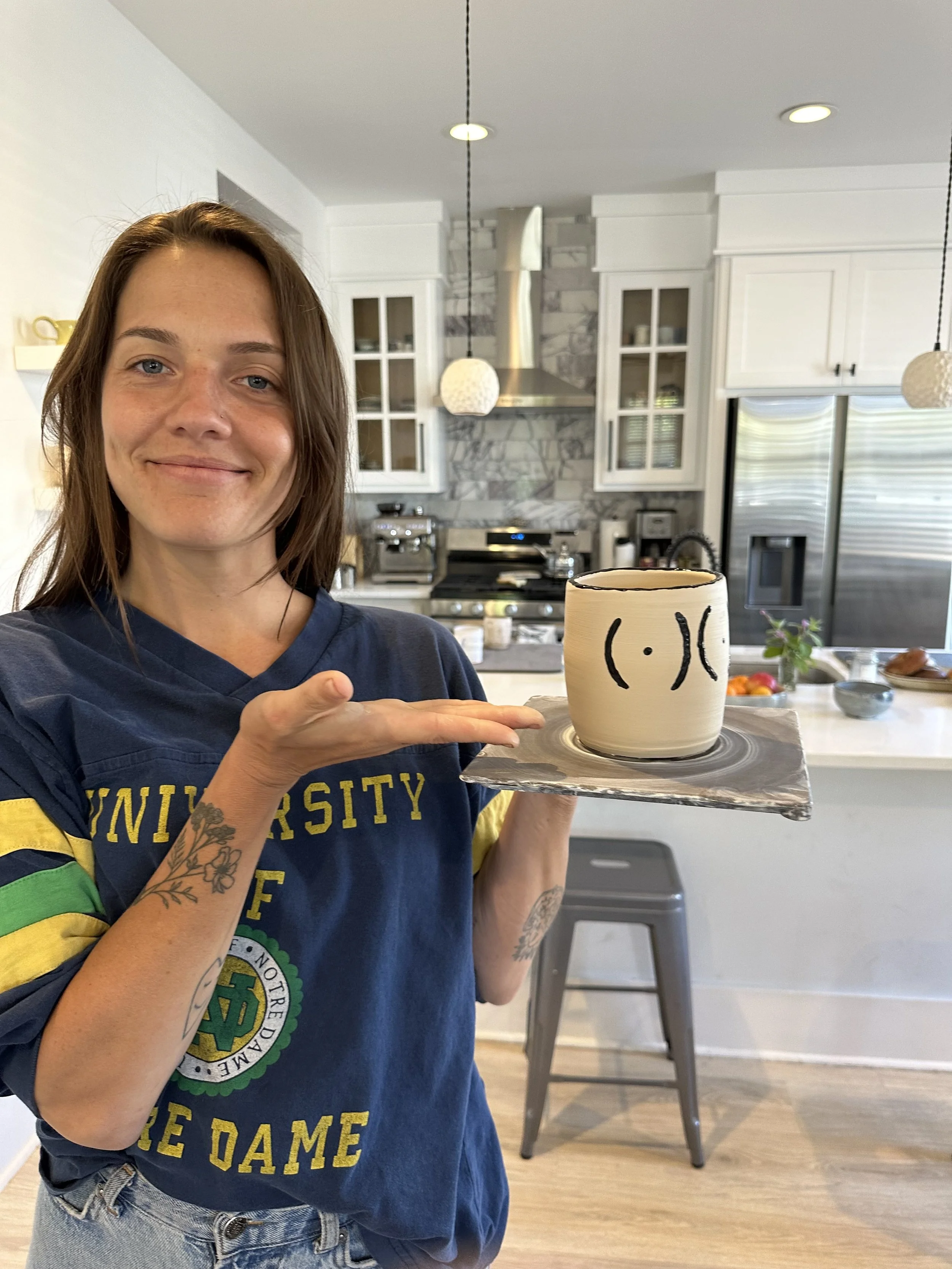 A person holding a mug in a modern kitchen, wearing a "University of Notre Dame" shirt and displaying a tattoo.