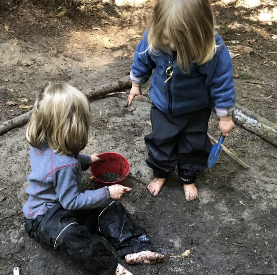 two barefoot children play in the mud with a shovel and bucket
