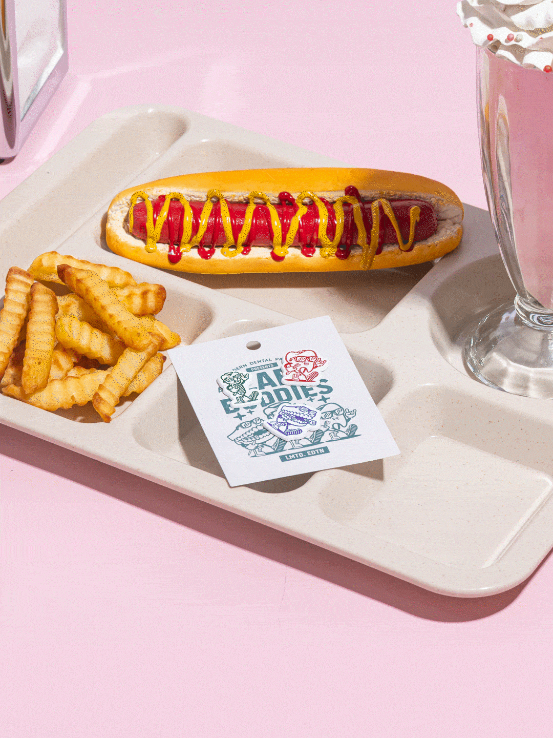 French fries, a hot dog with ketchup and mustard, and a card on a plastic tray, with a pink background.