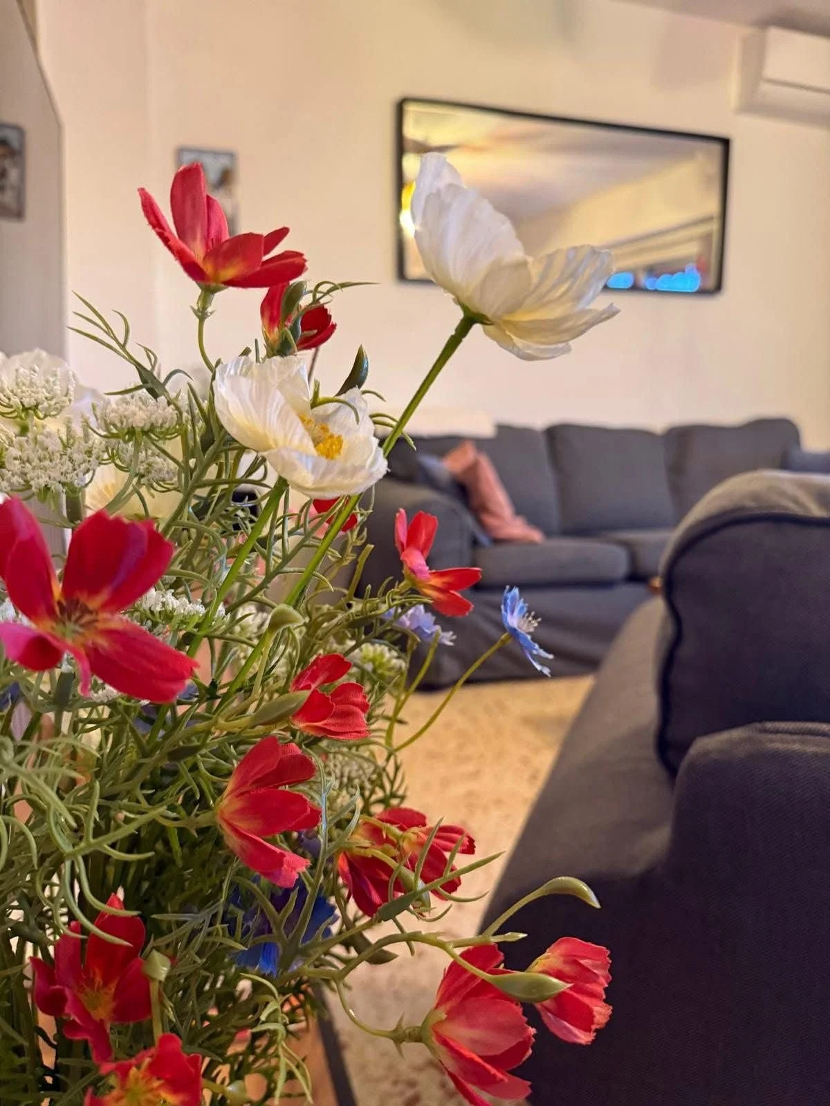 Bloemenboeket op de salontafel met zicht op de grijze zetel en spiegelwand in het vakantieappartement in Calpe.