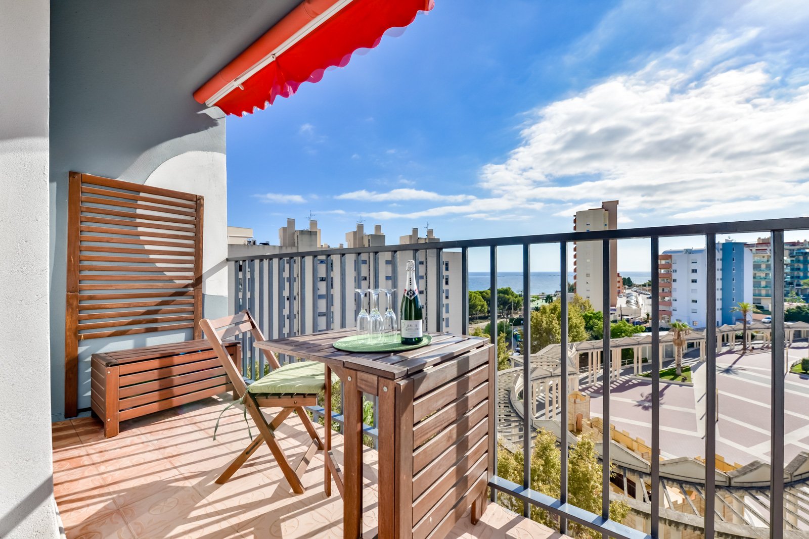 Terras van een vakantieappartement in Calpe met cava op tafel, houten stoelen en uitzicht op zee en de stad.