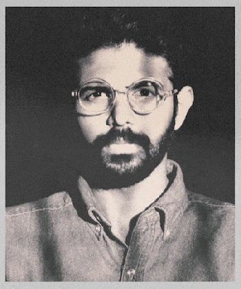 Black and white portrait of a man with glasses, a beard, and short curly hair, wearing a collared shirt.