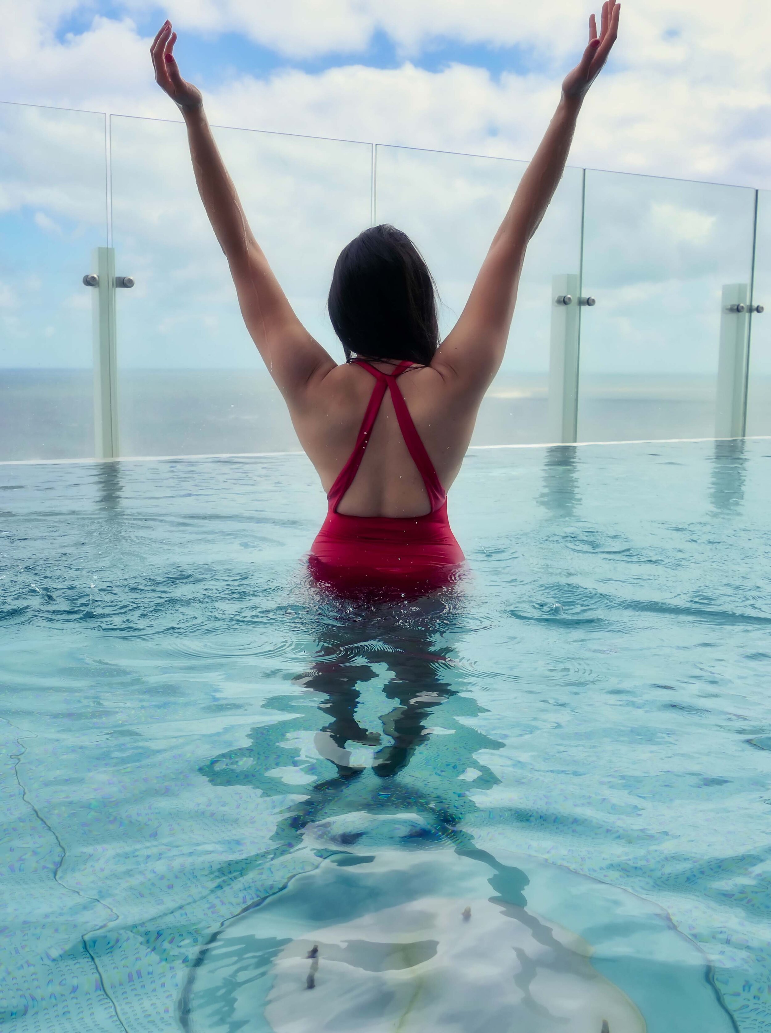 Here you see Escort Maya in an infinity pool with red swimming costume overlooking the sea.