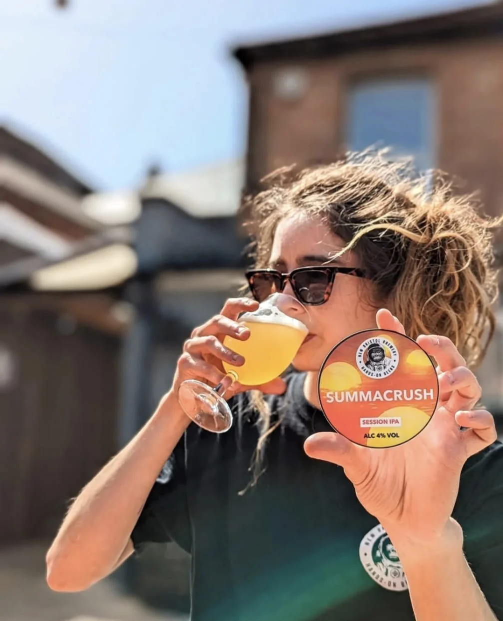 Woman drinking a beer and holding a tap badge in the sun