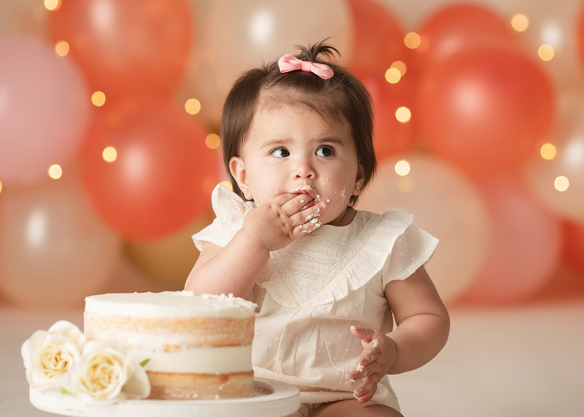 baby girl eating cake with balloon backdrop