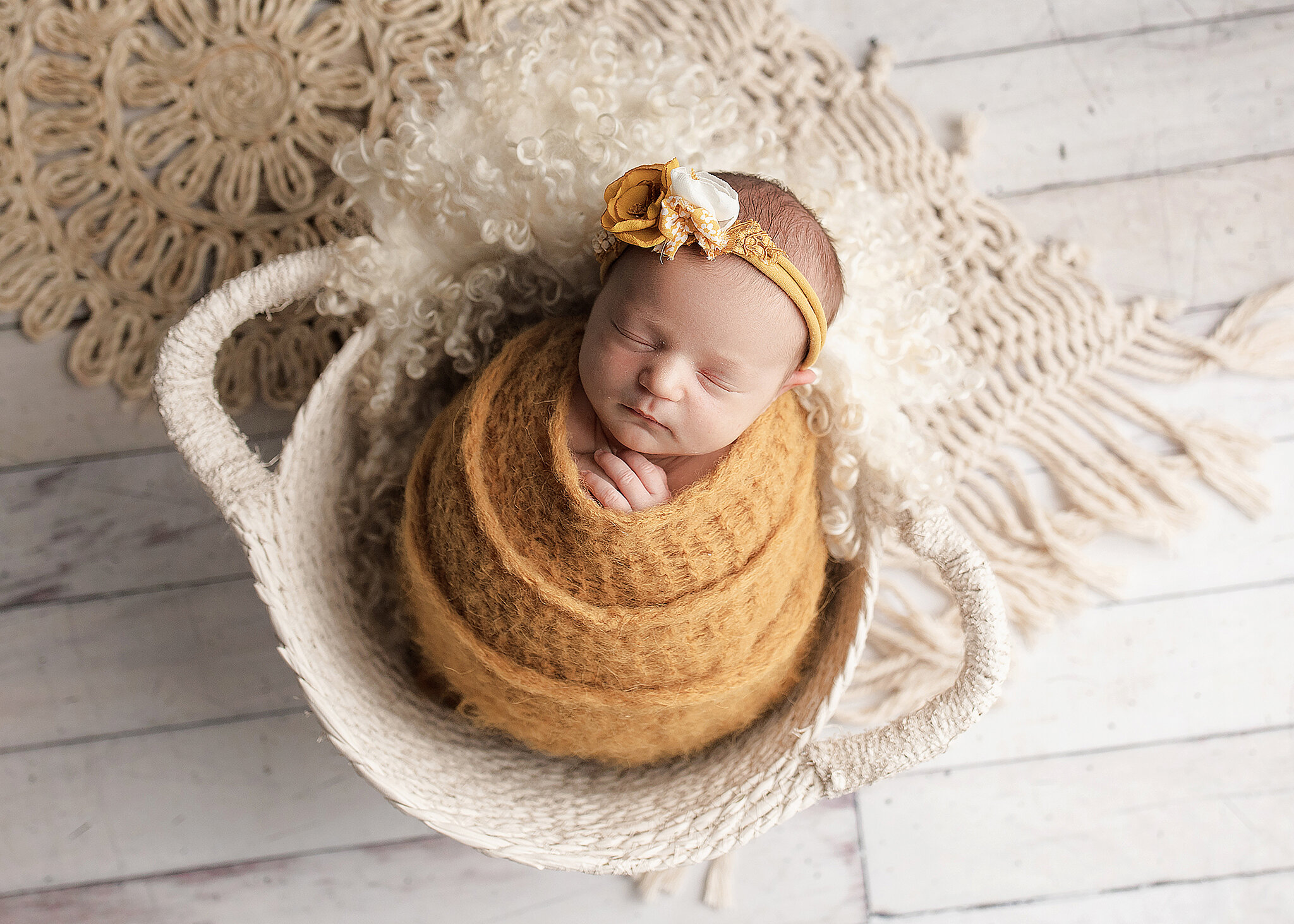 newborn girl in yellow swaddle asleep in white basket