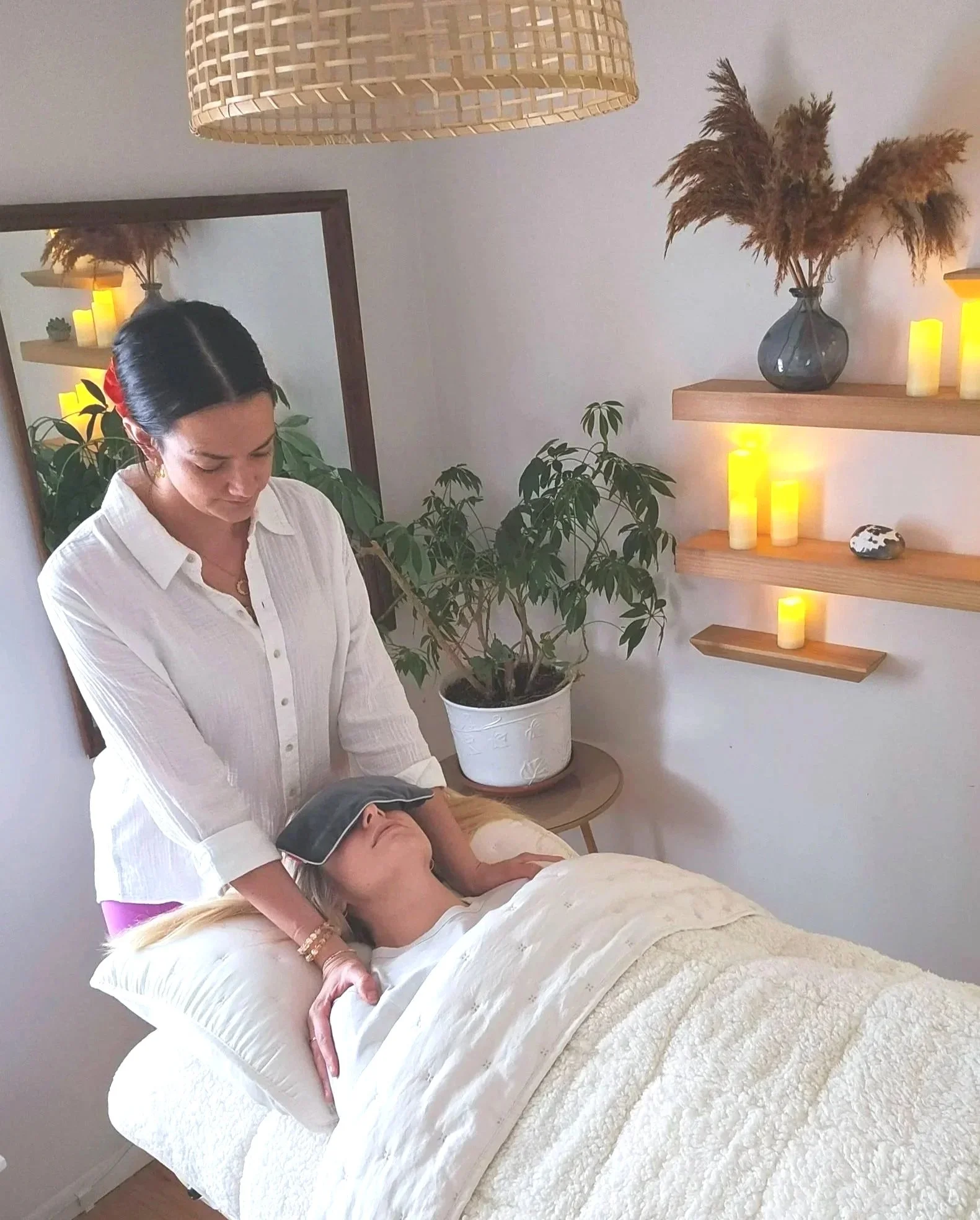 Sophie, Founder of HER,  giving a Reiki session to a person lying on a massage table in a calming room with plants and candles.