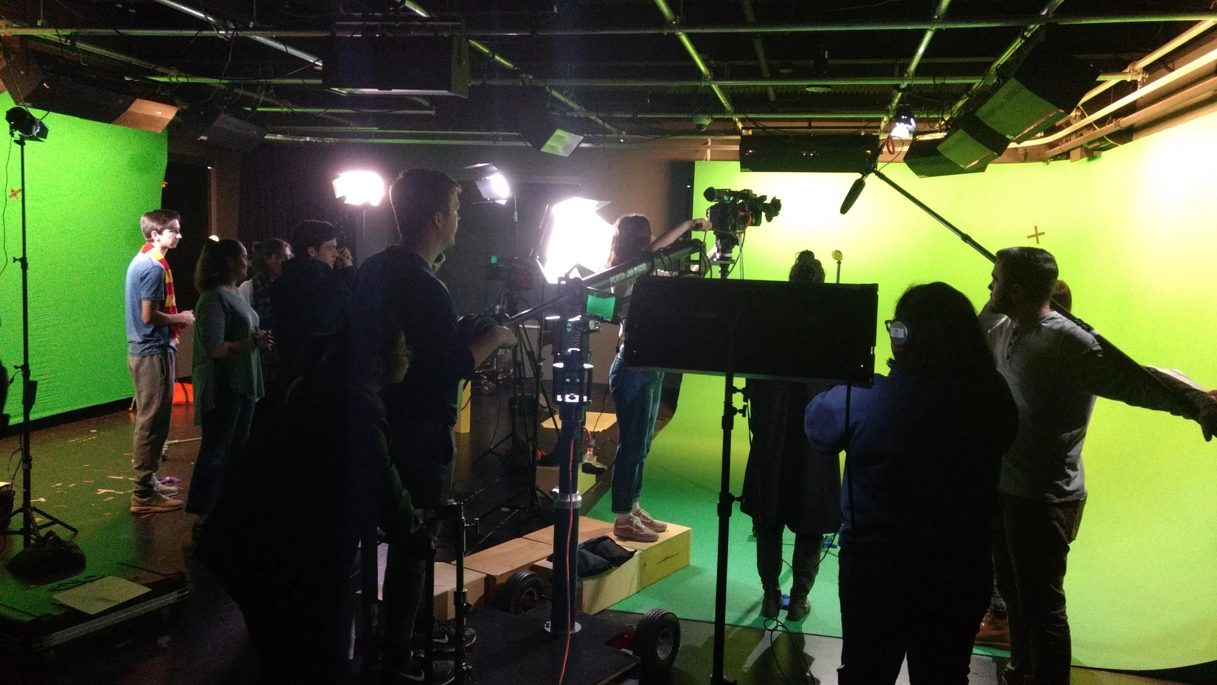People working on a film or video production set with a green screen in the background and various cameras and lighting equipment.