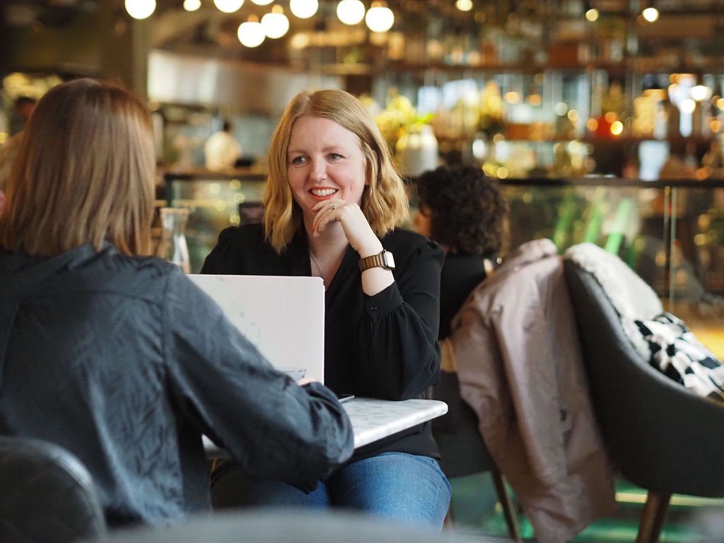 Lee in a cafe, talking to a client who has their back to camera