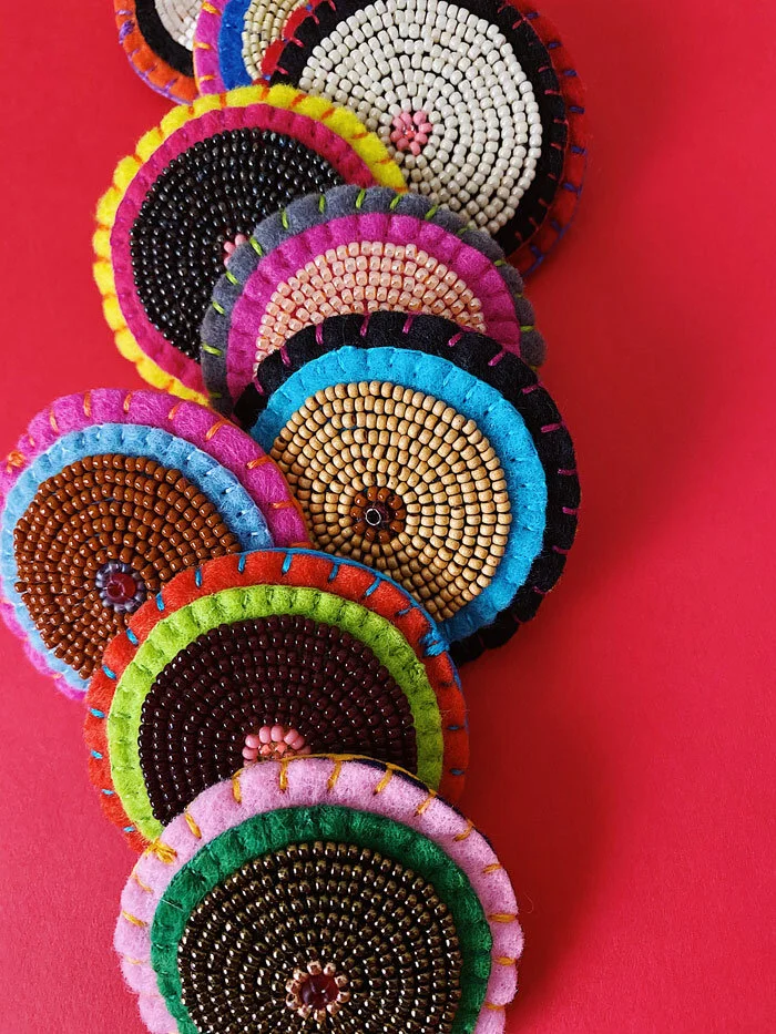 Close up group photo of colorful hand-sewn & beaded felt brooches of various "skin tones" that looks like tatas.