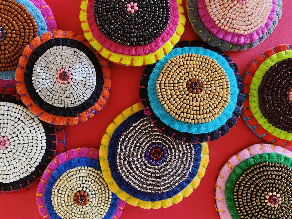 Overview group photo of colorful hand-sewn & beaded felt brooches of various "skin tones" that looks like tatas.