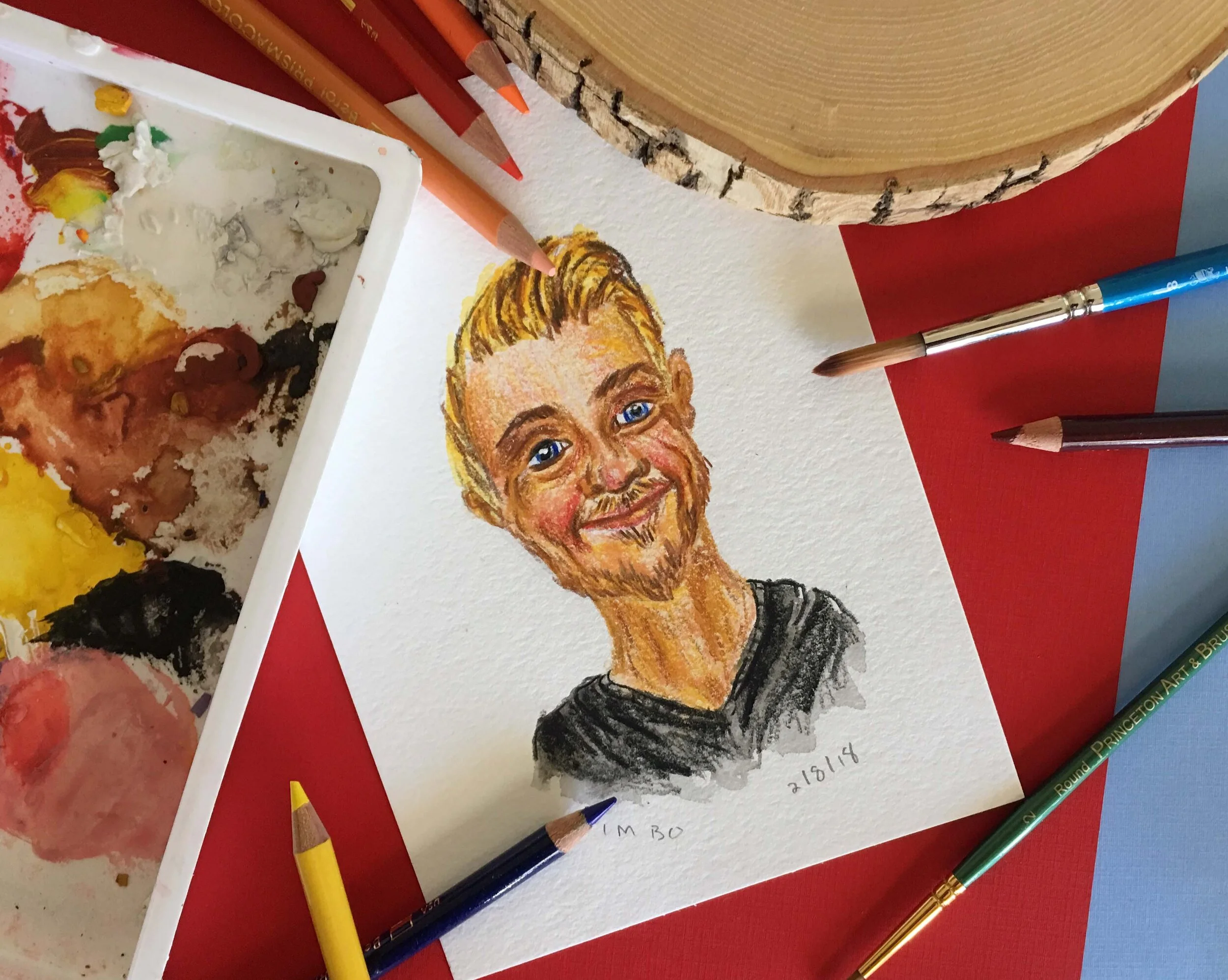 Portrait of a man using gouache and colored pencils on a red and blue background surrounded by art supplies.