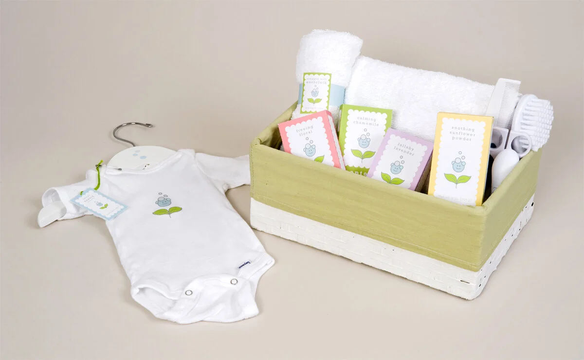Group photo of products: It contains a baby onesie, and a basket with soaps, shampoo, towel, and baby grooming products.