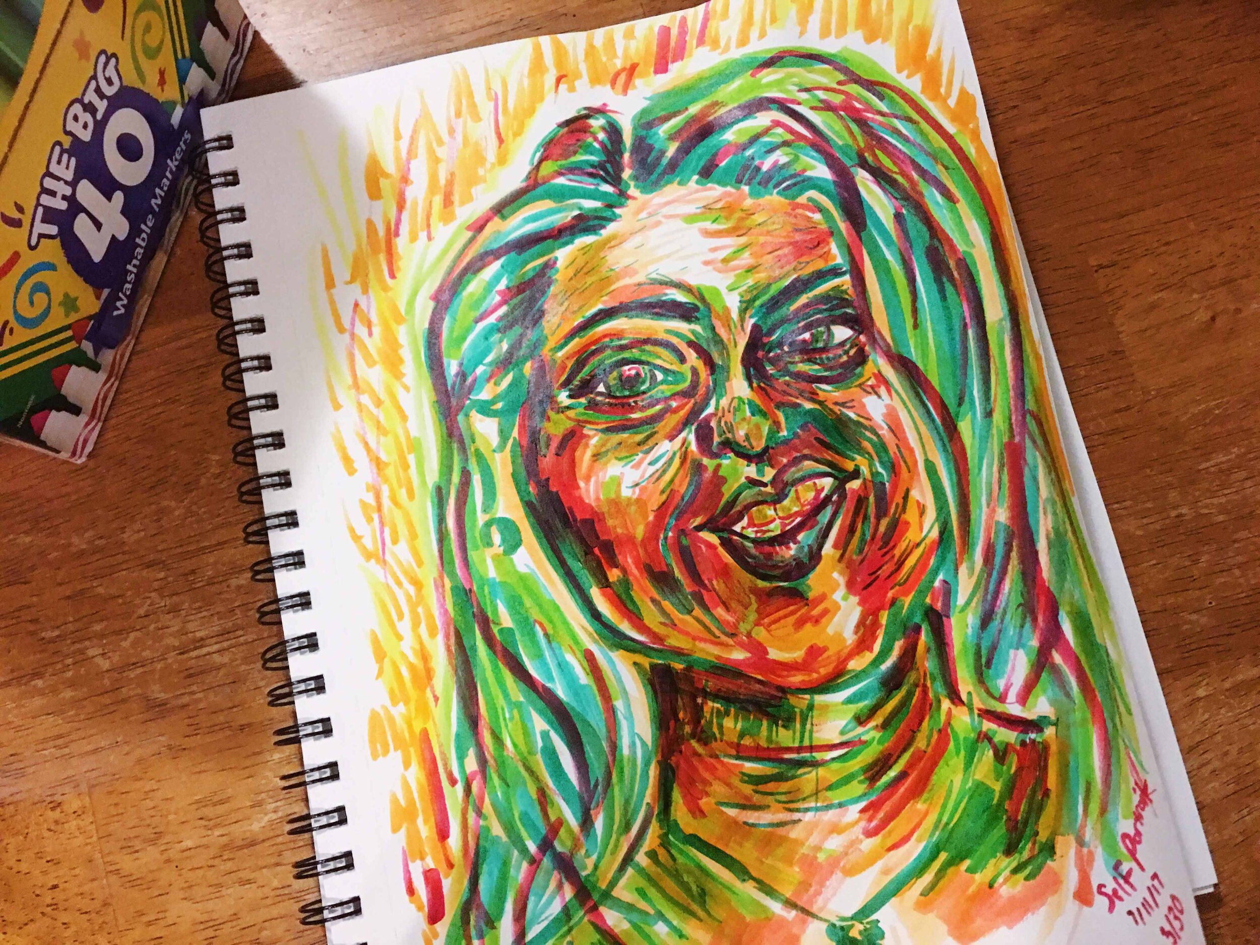 Day 3: photo of a self-portrait using markers surrounded by art supplies on a table.